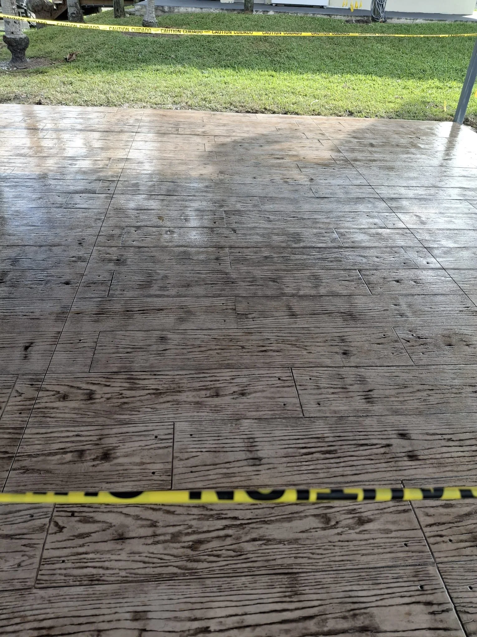 Wet wooden flooring behind caution tape, with a grass lawn in the background.