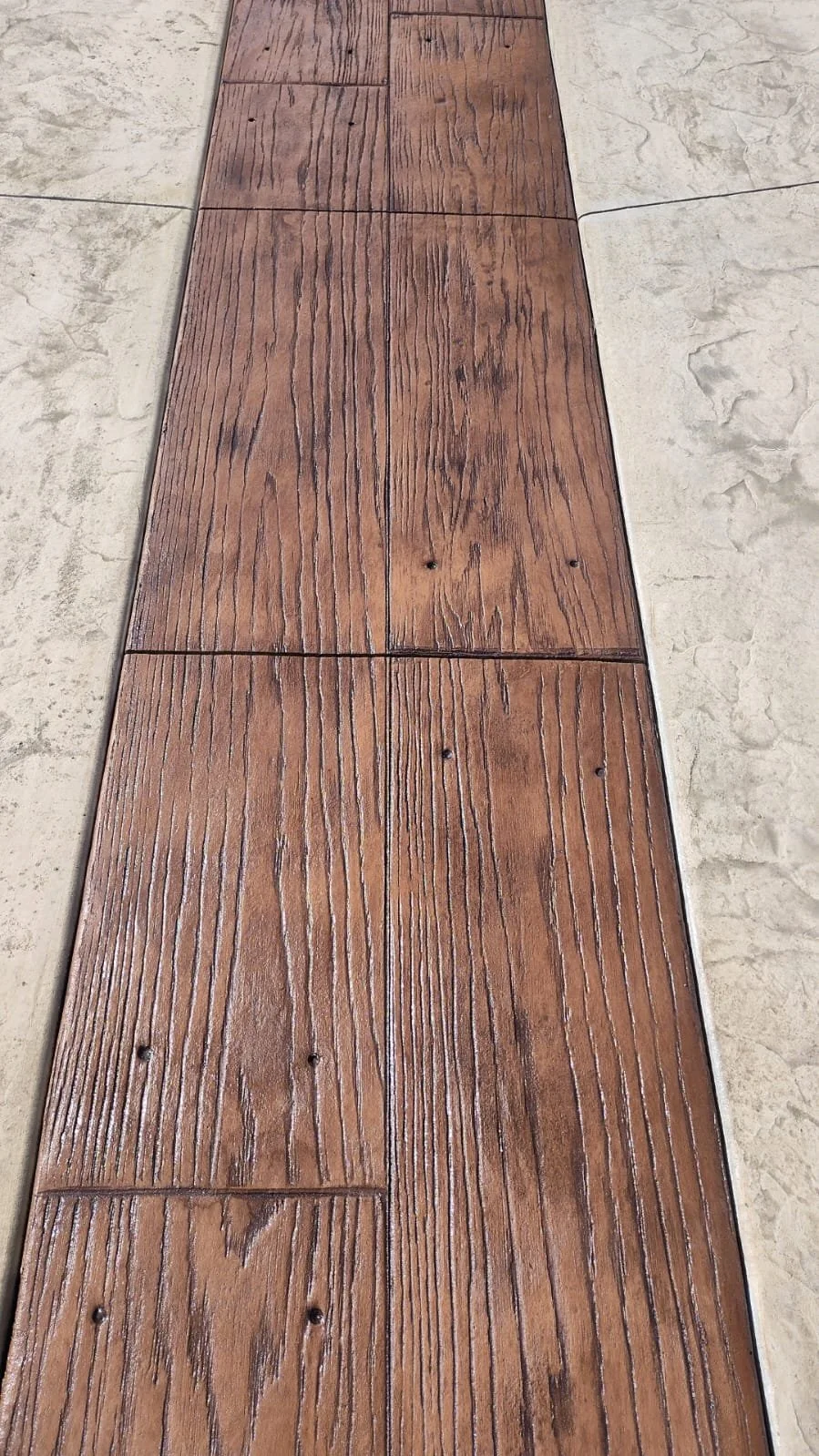 Wood-textured stamped concrete path with realistic grain details, flanked by lighter stone textured concrete on both sides.