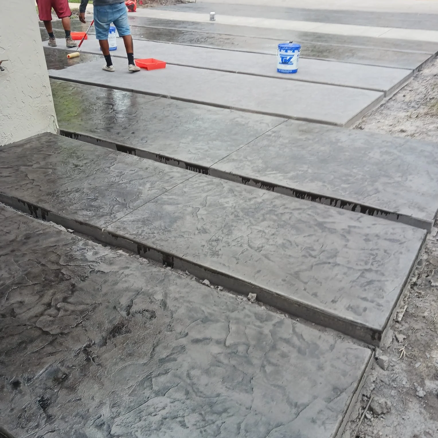 Workers applying a finish to newly poured stamped concrete walkway.
