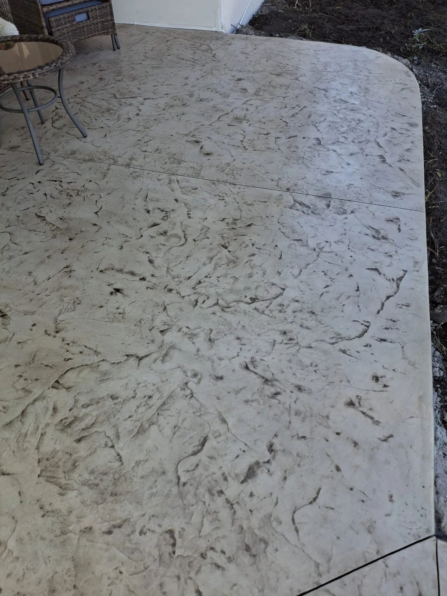 Textured concrete patio surface with a glass-top wicker table and chairs.