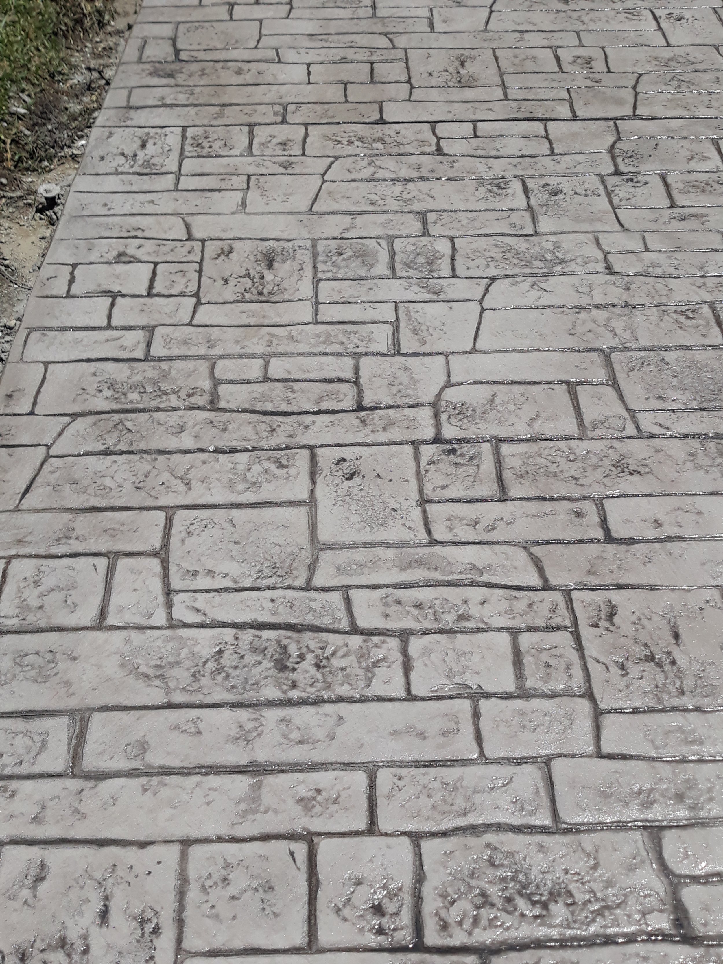 Patterned decorative stamped concrete pavement with a brick-like design and grey textured surface.