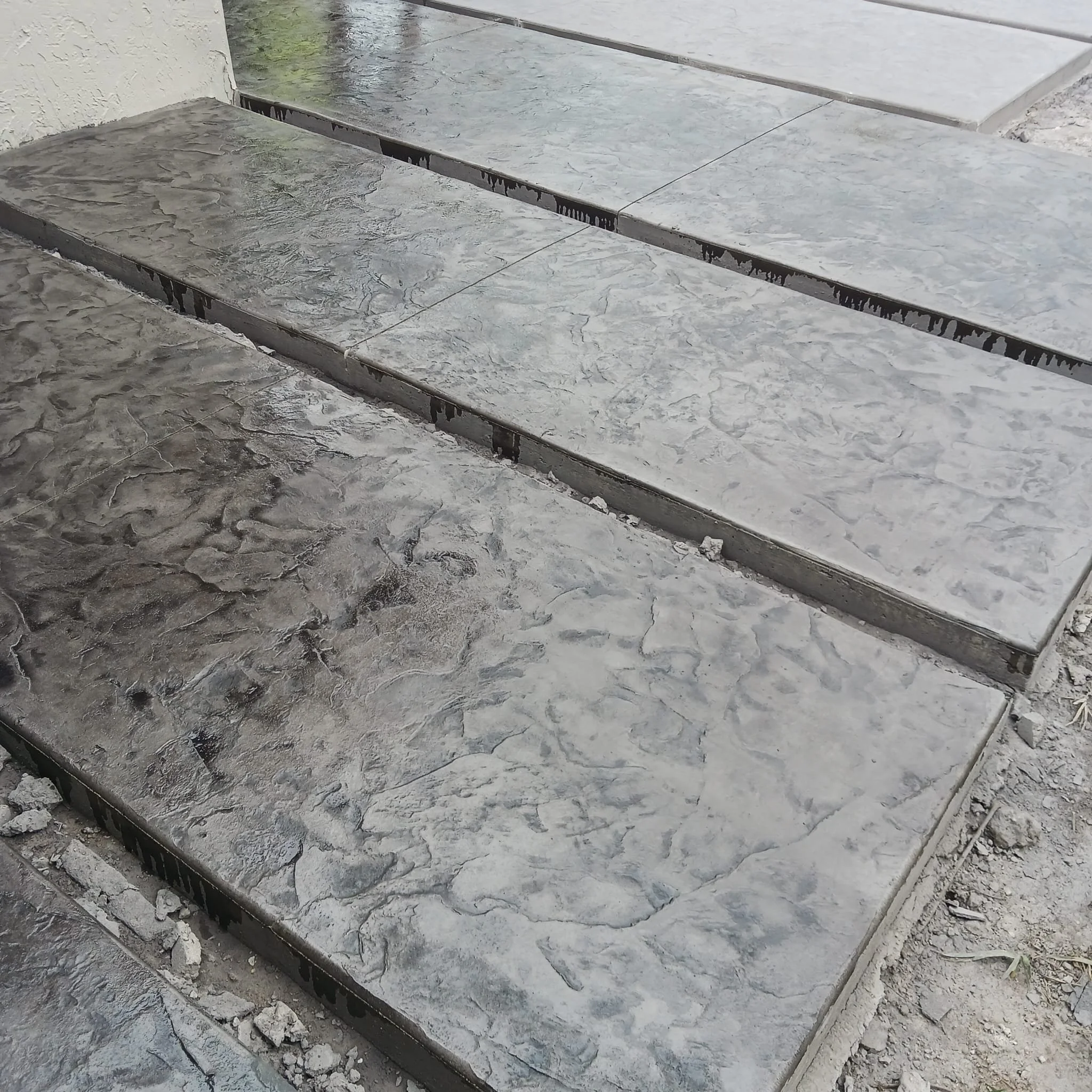Textured concrete steps with a wet appearance and surrounding gravel.