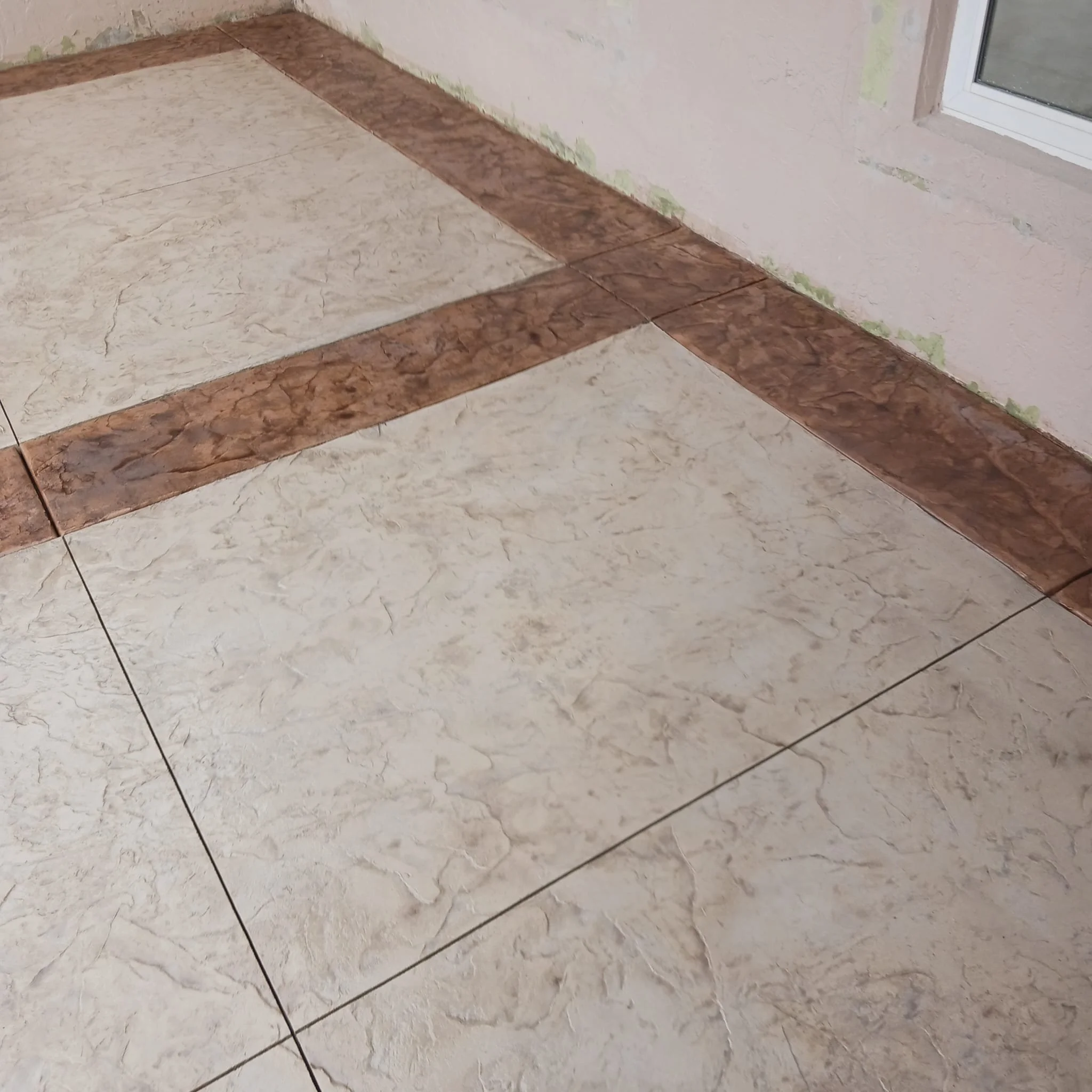Tiled floor with beige and brown patterned tiles next to a wall with a window.