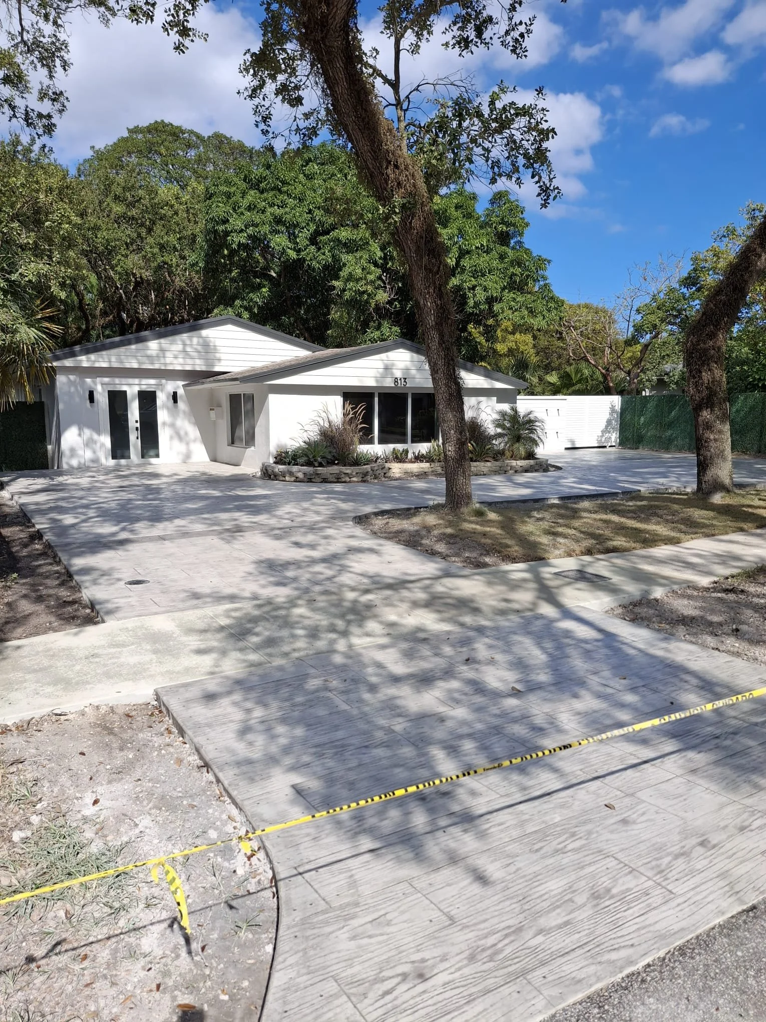 Single-story white house with large driveway and trees; caution tape across the bottom of the driveway.