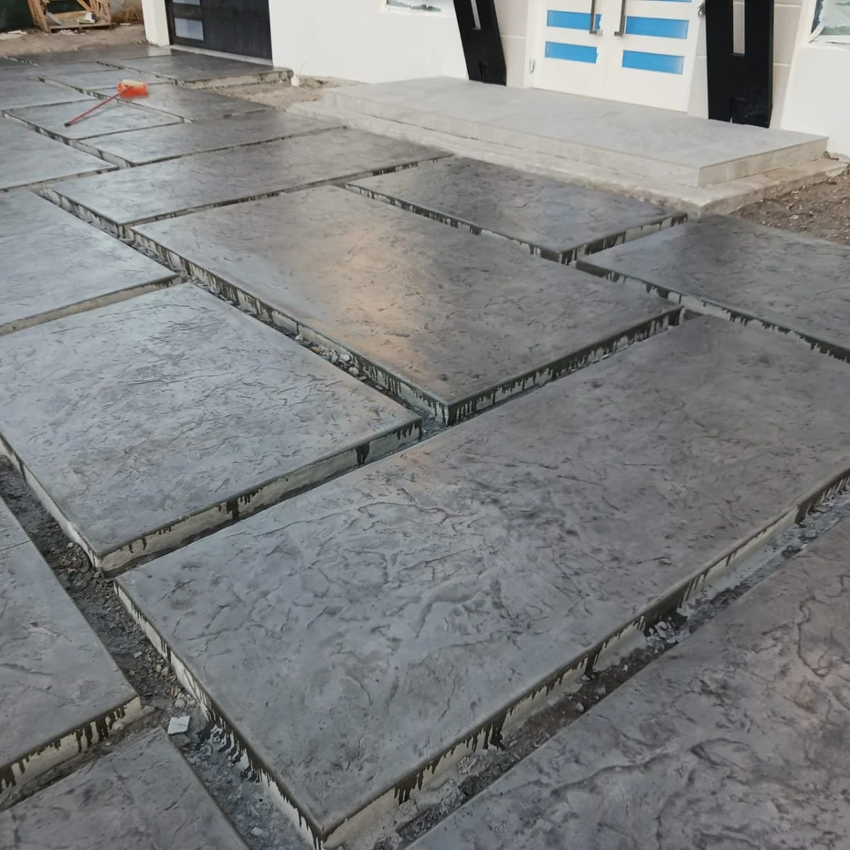 Stamped concrete driveway with rectangular slabs near a building entrance.