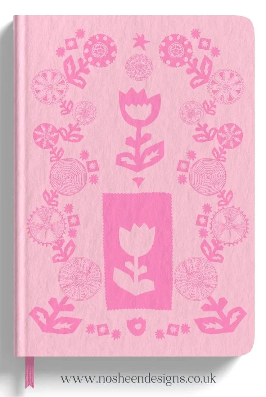 A pink notebook with floral and geometric patterns on the cover in darker pink, including tulip-like flowers and circular designs, and a website URL www.nosheendesigns.co.uk at the bottom.