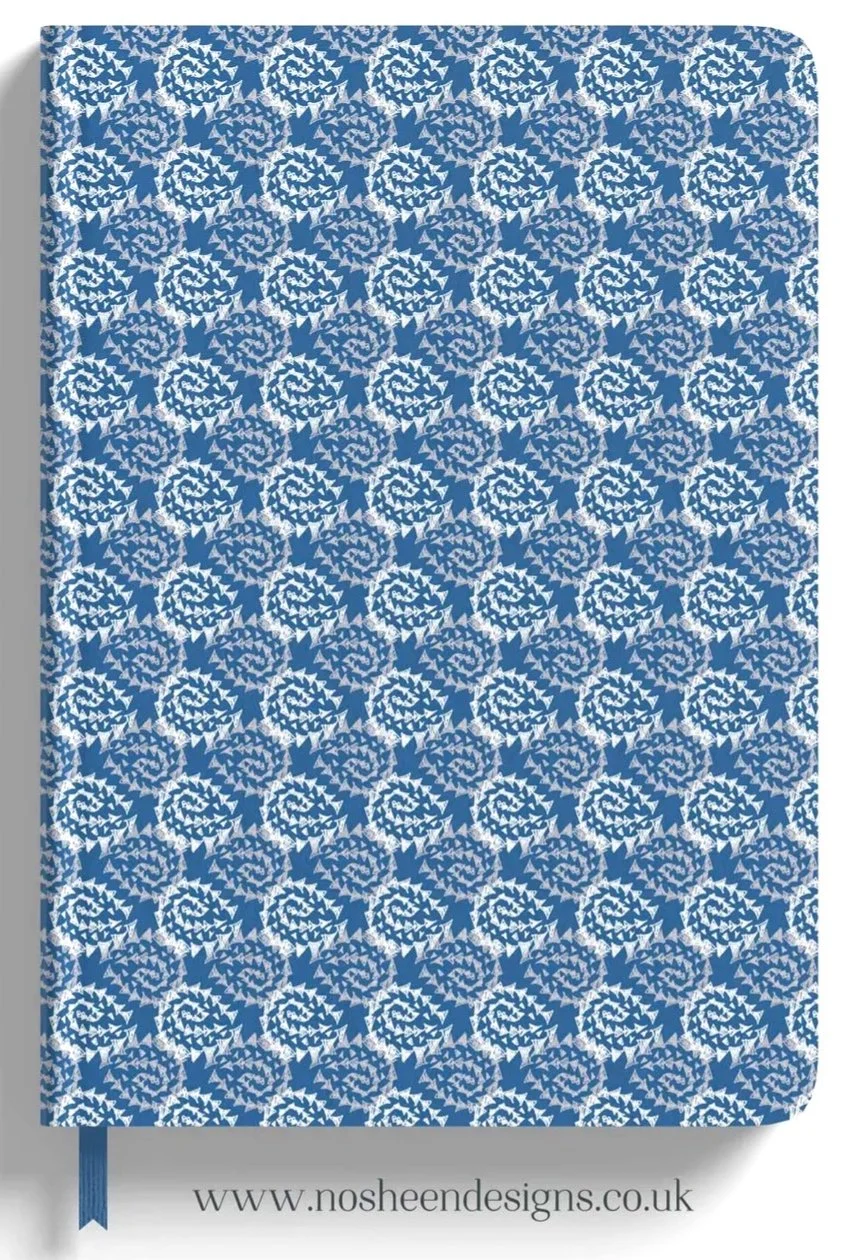 A notebook cover with a blue and white geometric spiral pattern. The bottom features a website URL, www.nosheendesigns.co.uk, and a blue ribbon bookmark.