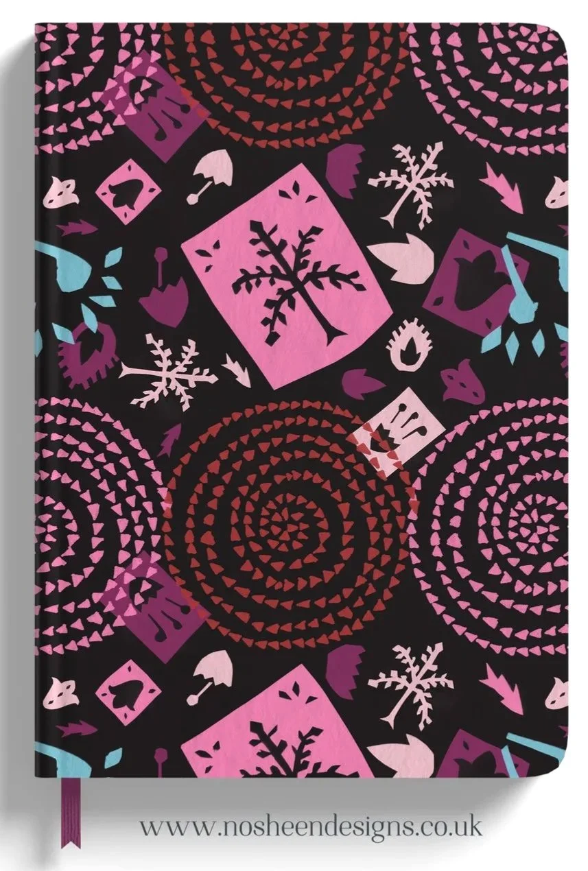 A black notebook cover with pink, purple, and blue holiday-themed patterns including snowflakes, hearts, Christmas trees, and circular spiral designs, along with the website 'www.nosheendesigns.co.uk' at the bottom.