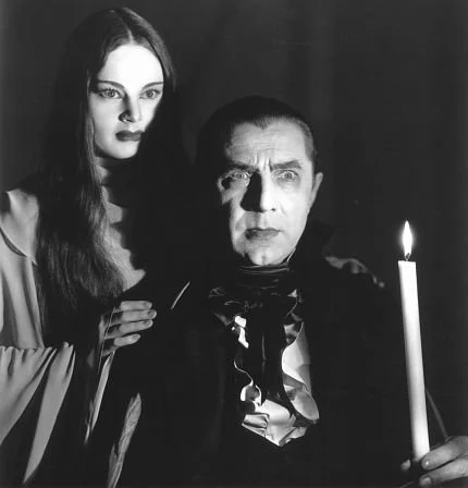 Black and white. Luna stands behind the count's shoulder. He holds a camera up. Both look off into the distance.
