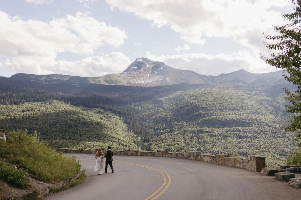 A bride and groom frolic along a pullout in Glacier National Park during their adventurous mountain elopement.