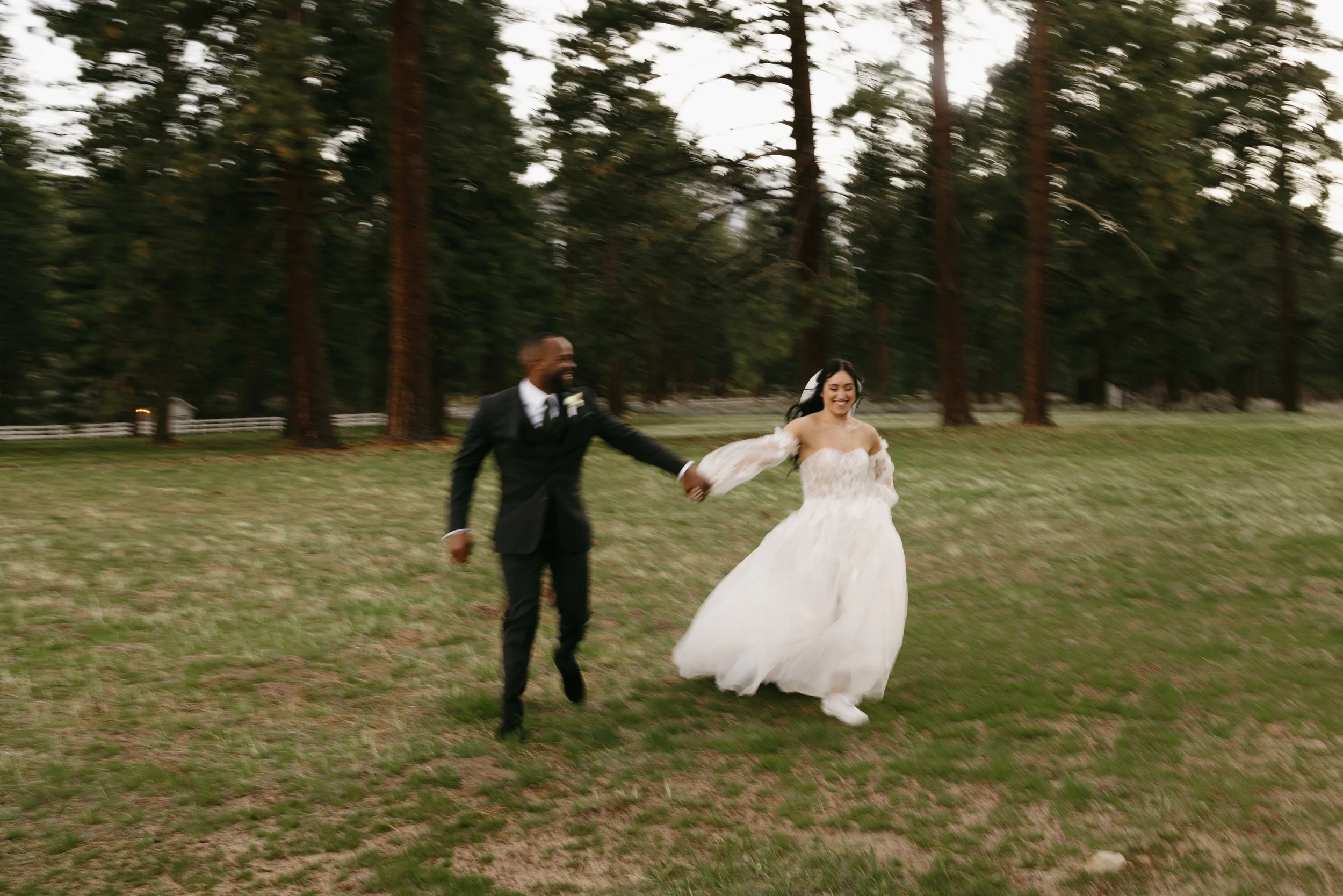 a bride and groom running towards the camera with blur motion and pine trees in the background