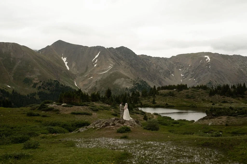 A bride and groom stand atop rocks in Loveland Pass during their intimate elopement photographed by Chuck and Shiloh.