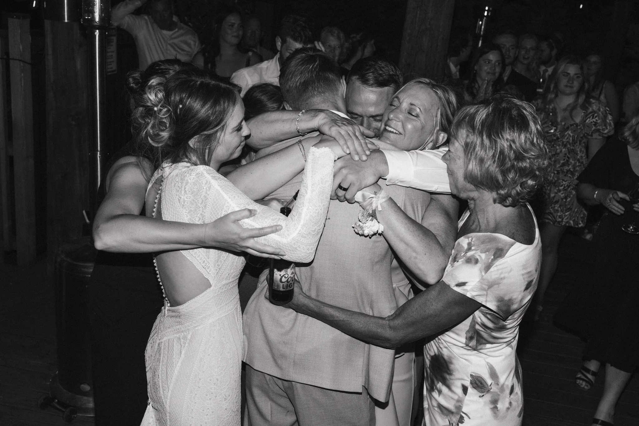 People hug and celebrate at a gathering, with smiles and affection, in a dimly lit setting.