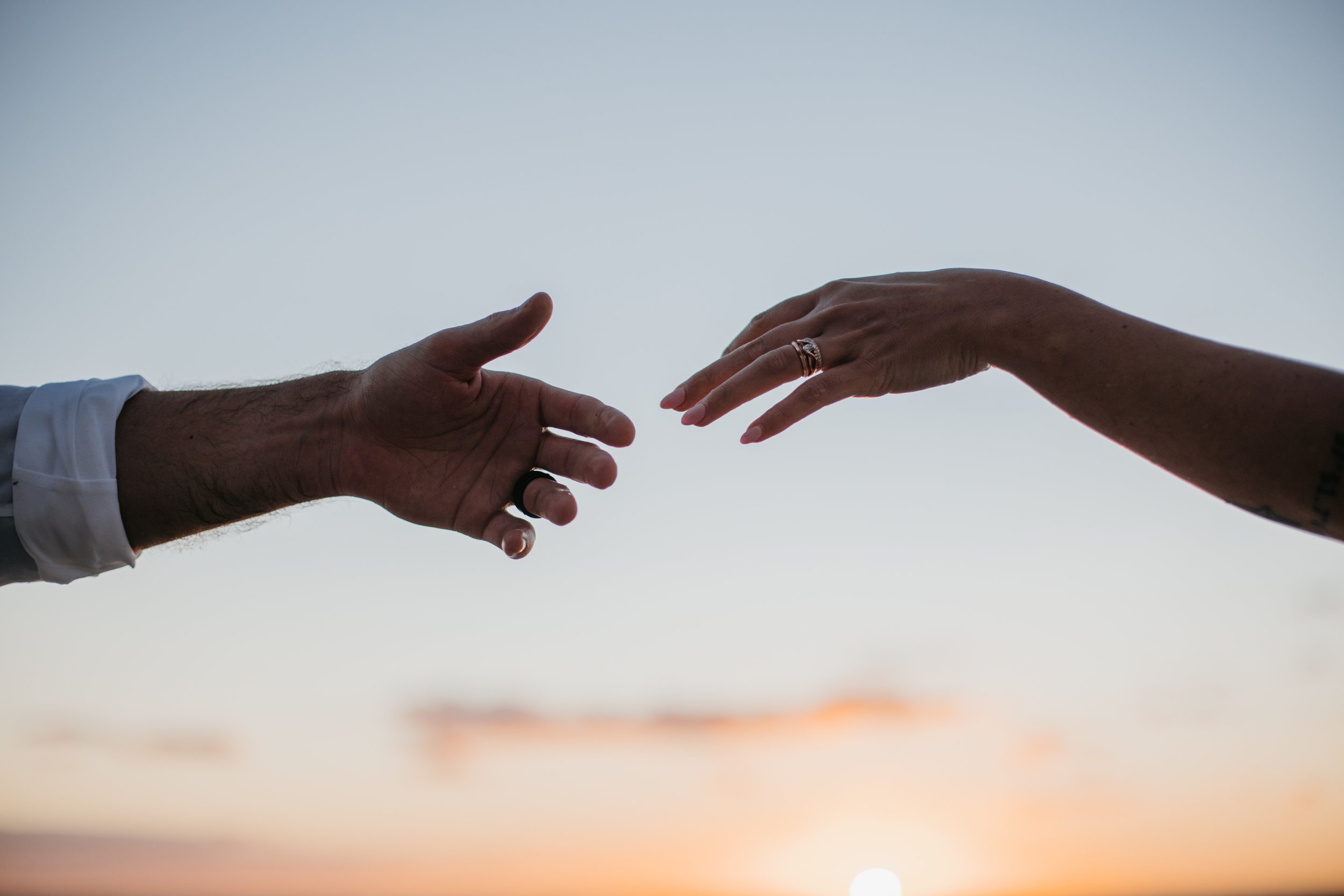 Two hands reaching towards each other against a sunset sky.