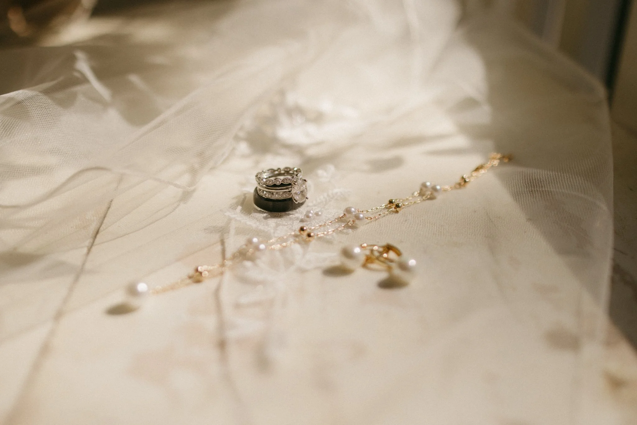 A collection of jewelry, including rings, necklaces, and earrings, laid out on a cream-colored fabric with sheer material nearby.