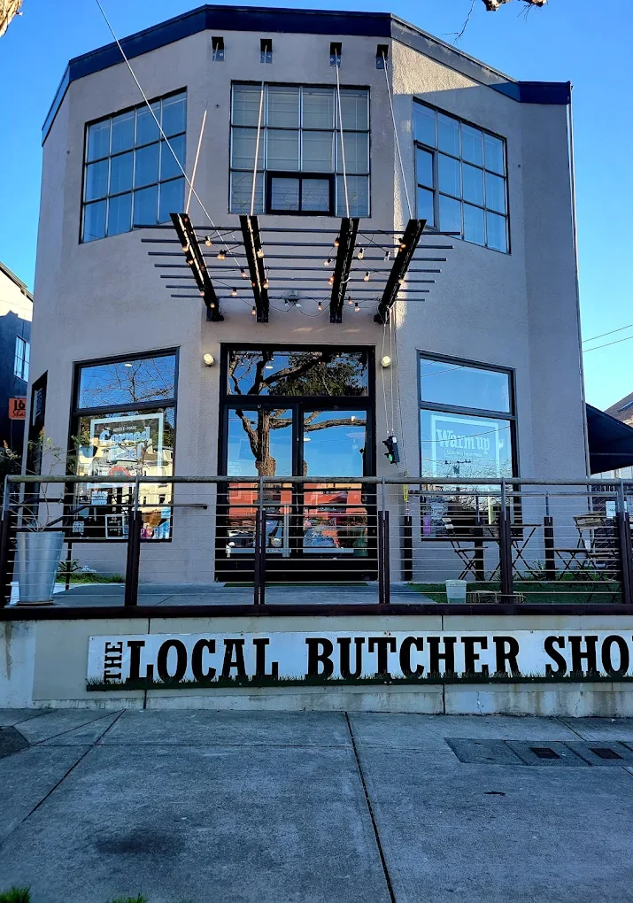 The exterior of a two-story building with large glass windows and a sign that reads 'The Local Butcher Shop'.