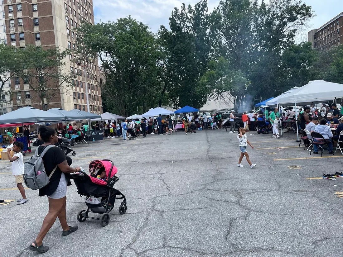 woman pushes stroller through a parking lot filled with tarps, tents, and tables crowded in a parking lot crowded with people at Kindness Party on August 12, 2023 at Glenmore Plaza.