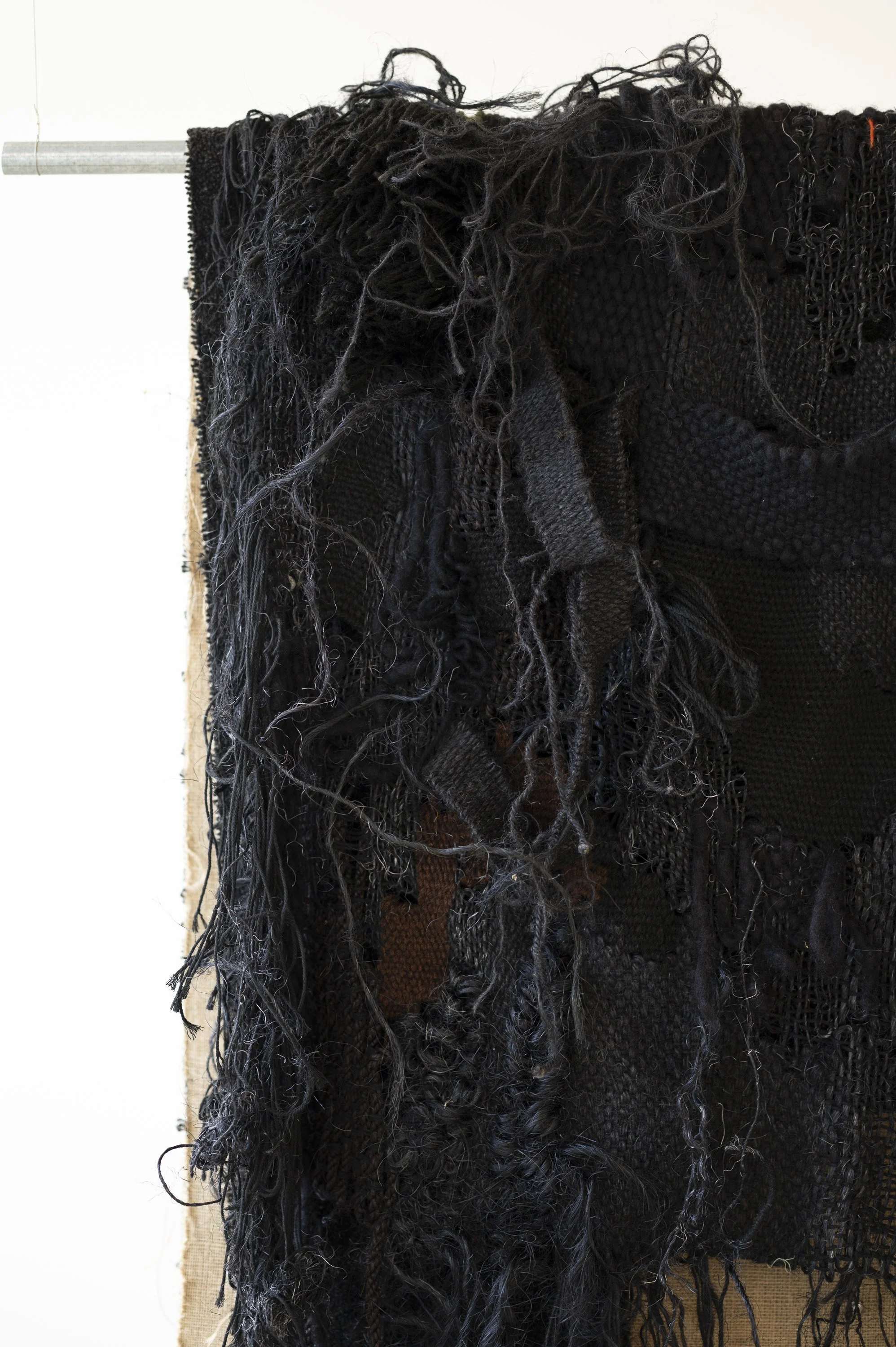 Hairy black handwoven wool, sisal and jute textile hanging on galvanised steel rail in a white gallery