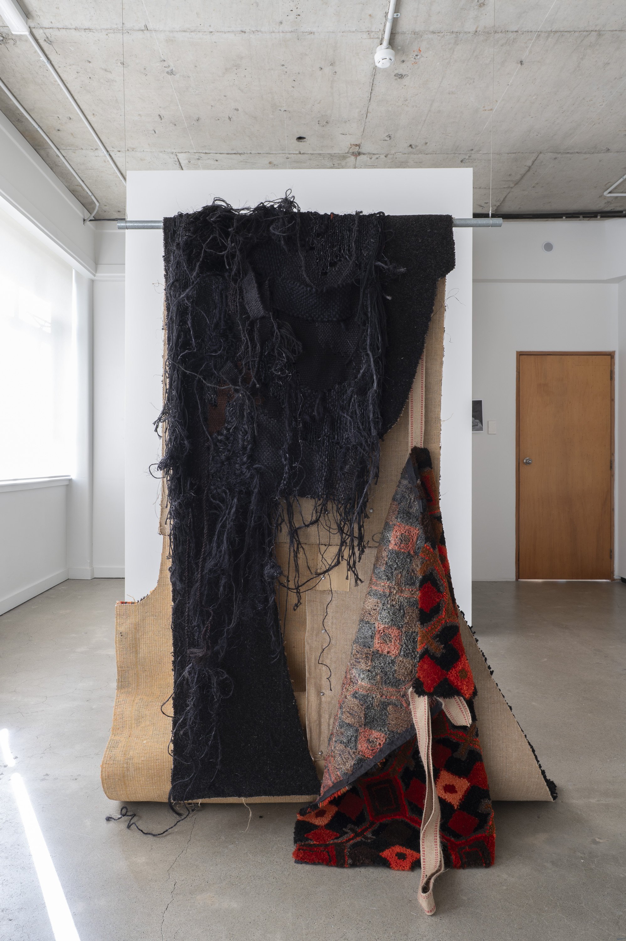 Large hanging sculpture made of a collage of hand tufted and commercial carpet in a black and orange
