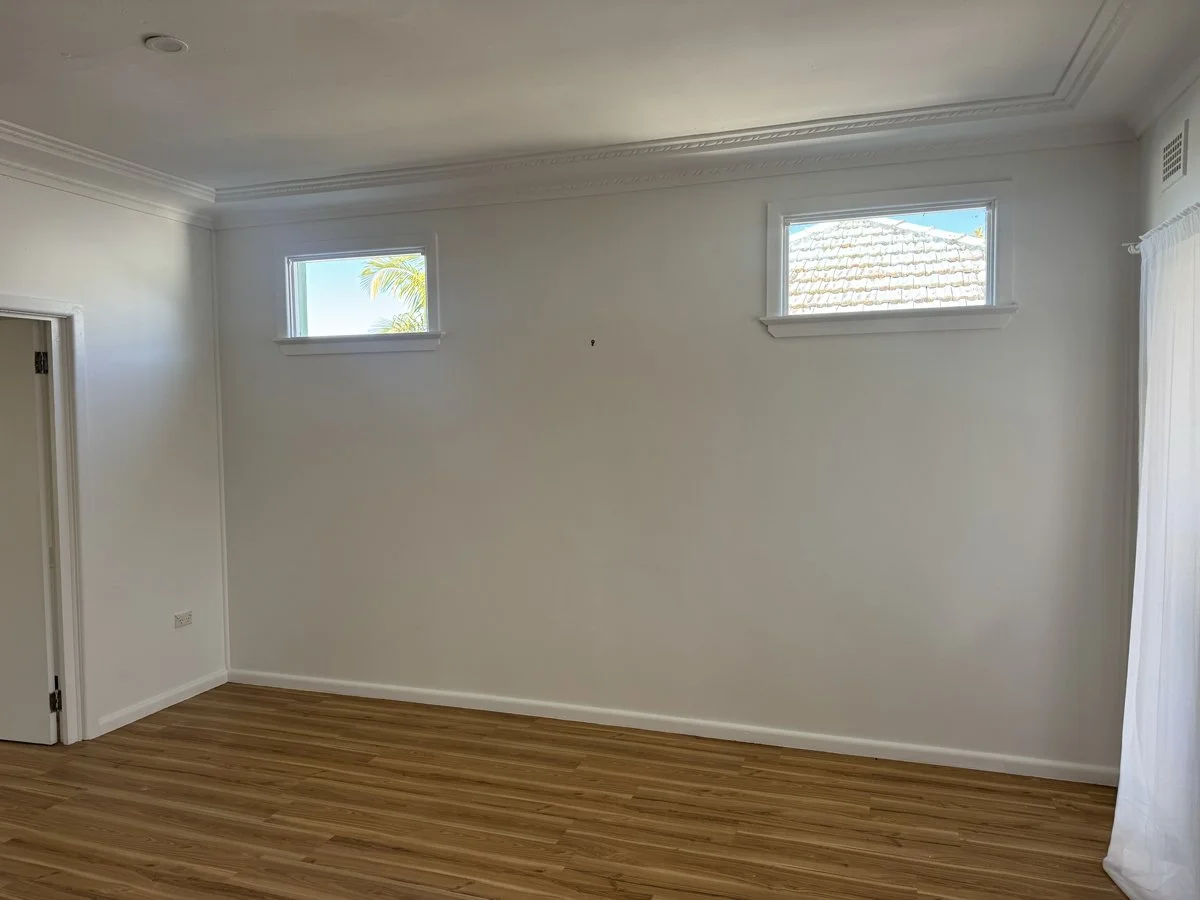 Empty room with black accent wall, beige curtains, and a window with potted plants outside.