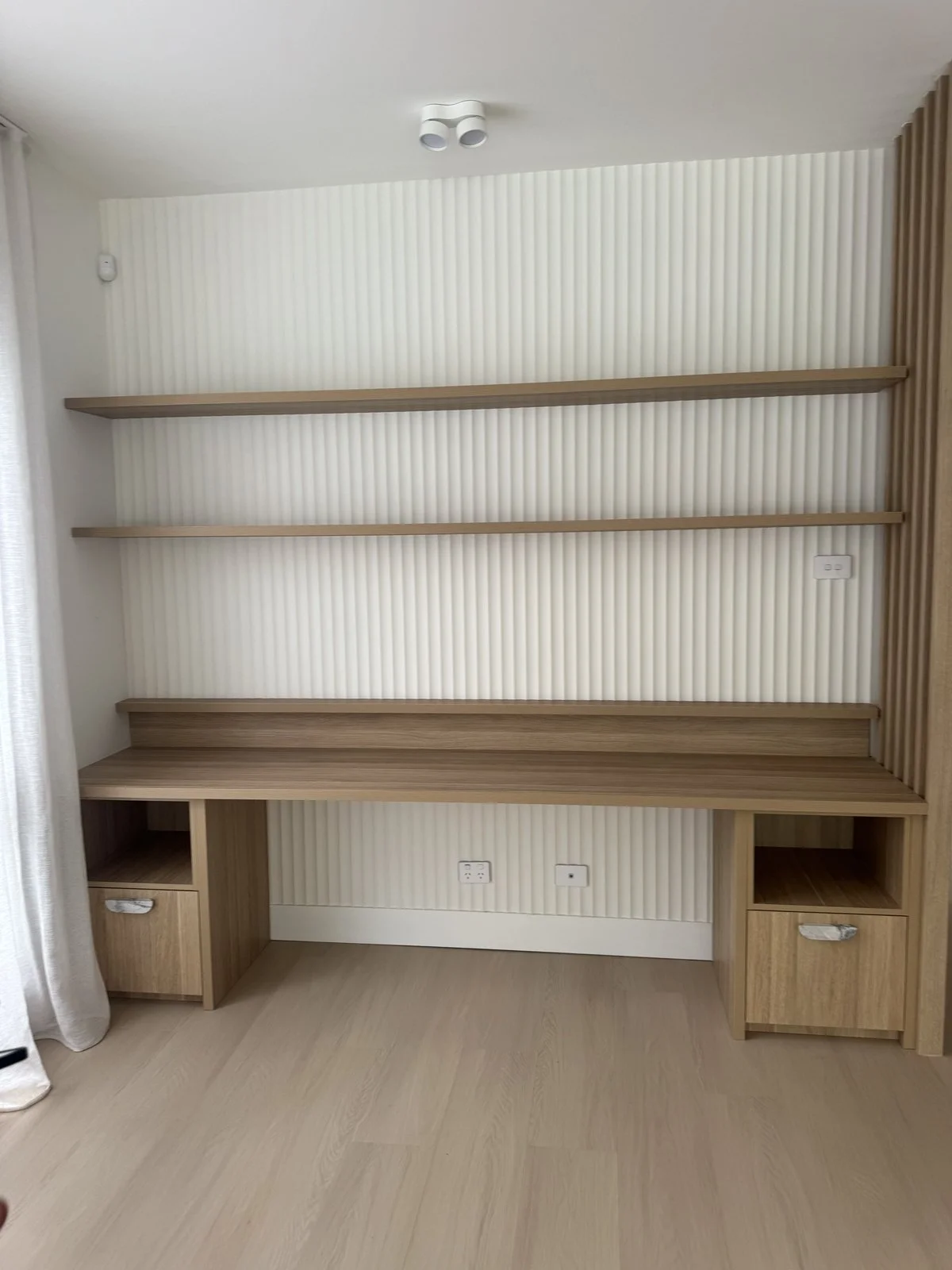 Empty wooden wall with three shelves, a built-in desk, and electrical outlets, in a modern room.