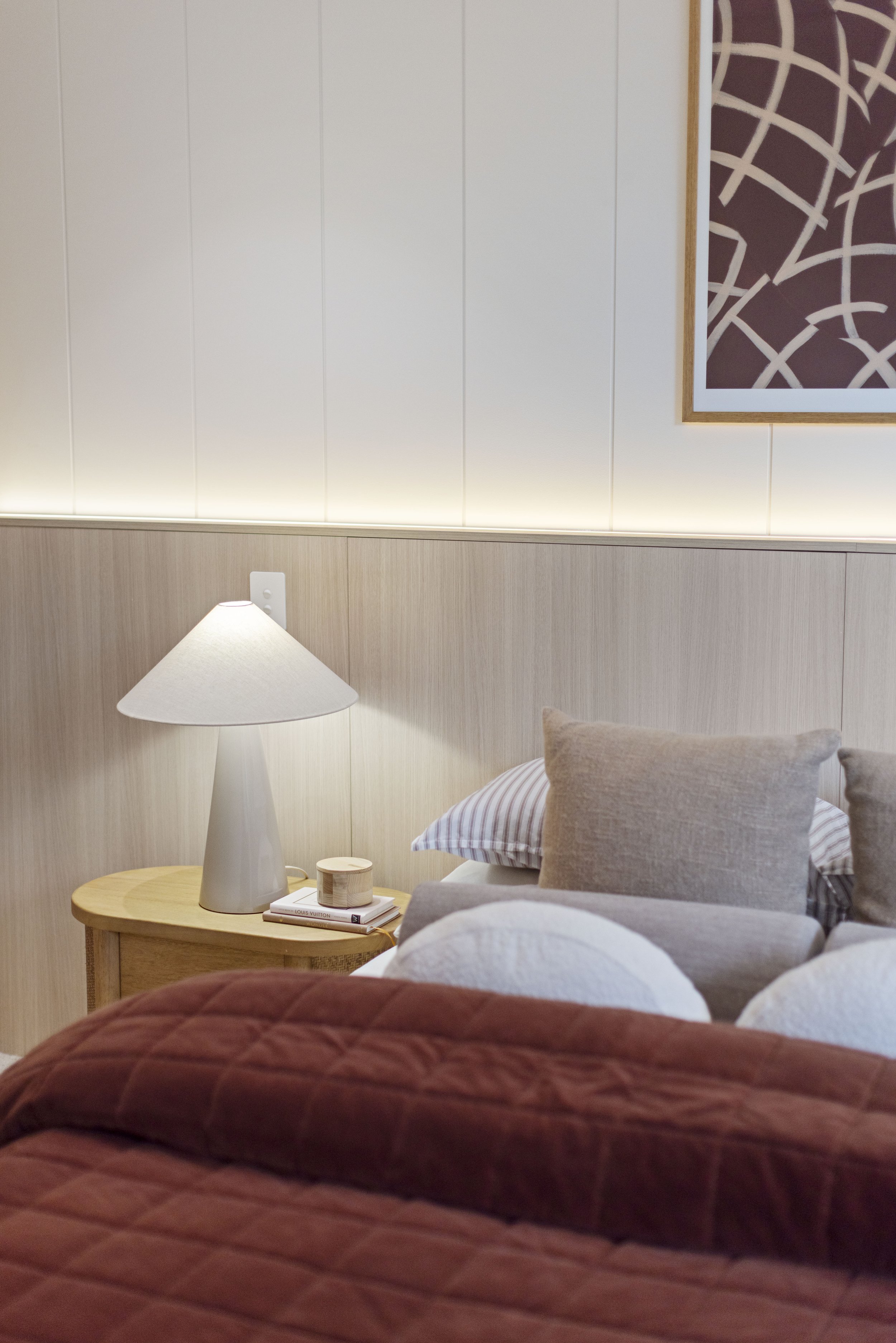 A bedroom with a bed, bedside table with a lamp, pillows, and wall art.