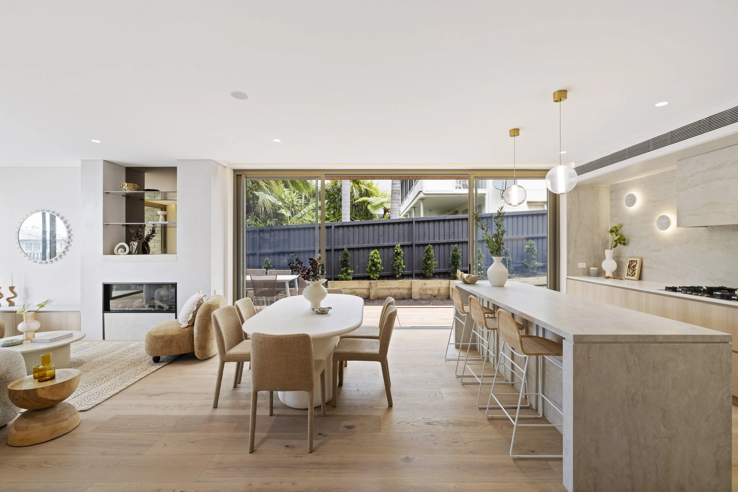 Modern open-plan living and dining area with large sliding glass doors leading to a backyard, featuring a beige color scheme, minimalist decor, and wooden flooring.