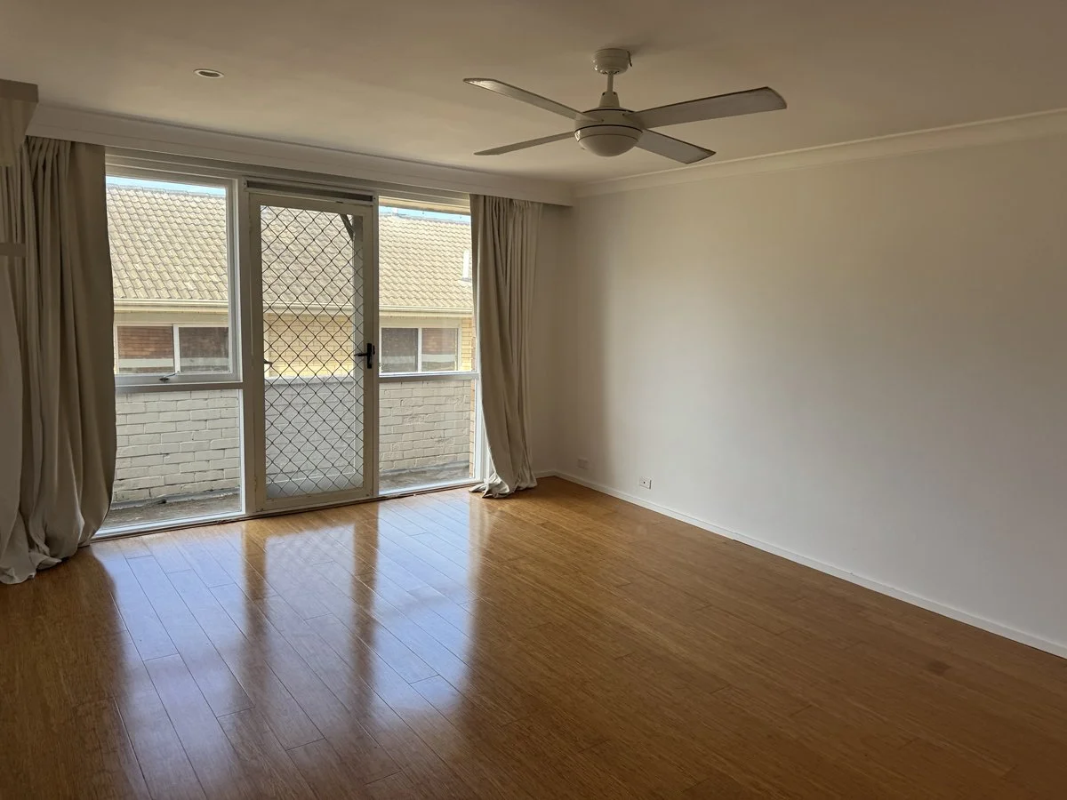 Empty room with black accent wall, beige curtains, and a window with potted plants outside.