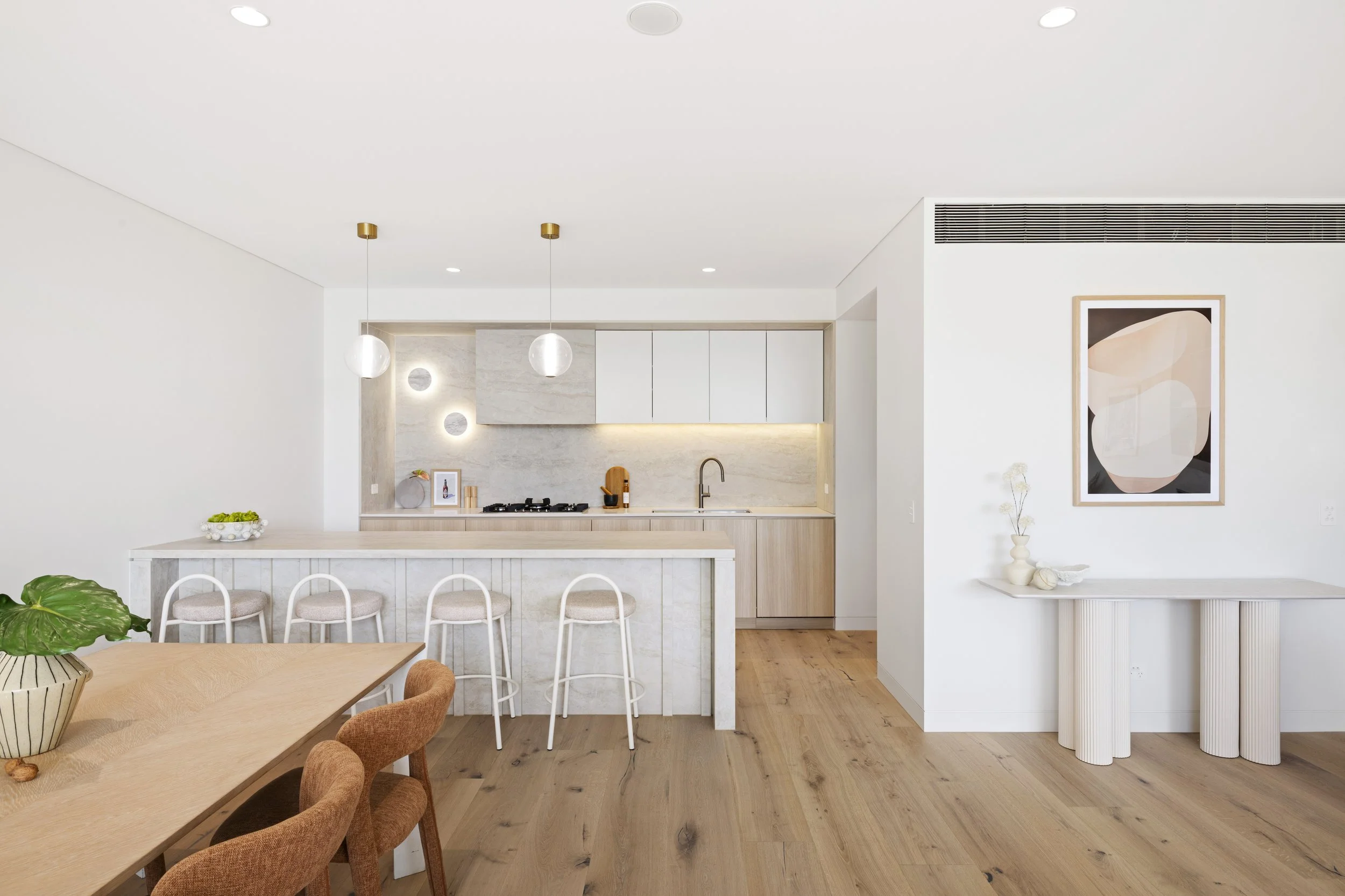 Modern kitchen with white cabinets, wooden accents, pendant lights, a wall art piece, and a wooden dining table with chairs.