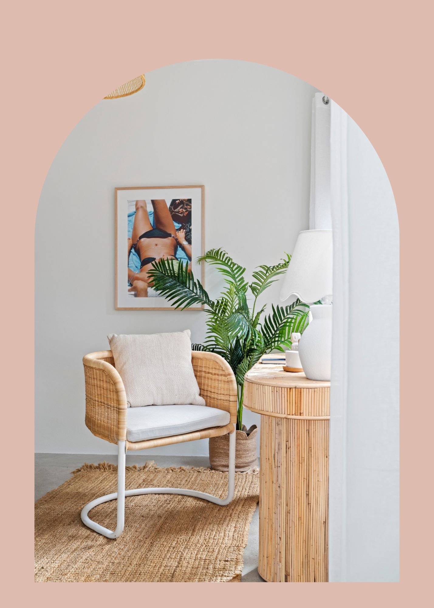 Interior of a cozy room with a rattan armchair with a cushion, a potted plant, a woven side table with books and a white vase, a lamp, a framed photo on the wall, a rug, and a curtain, with soft pastel wall colors.