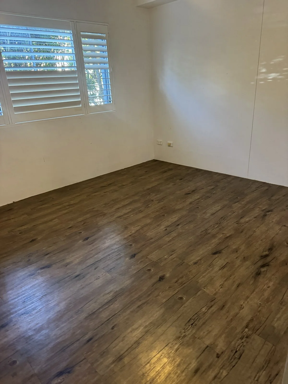 Empty room with black accent wall, beige curtains, and a window with potted plants outside.
