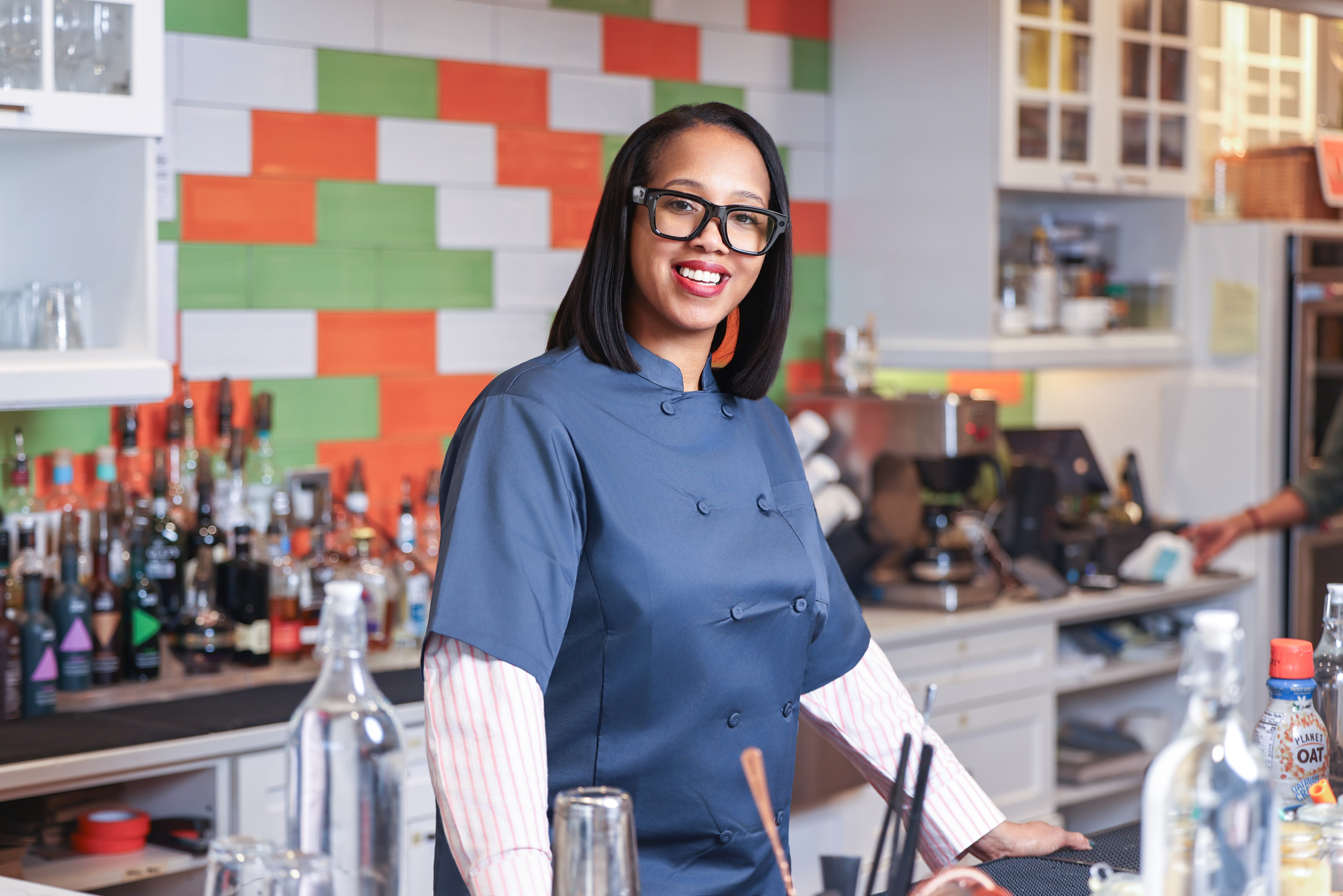 A female chef in a blue uniform smiling in a colorful restaurant kitchen.