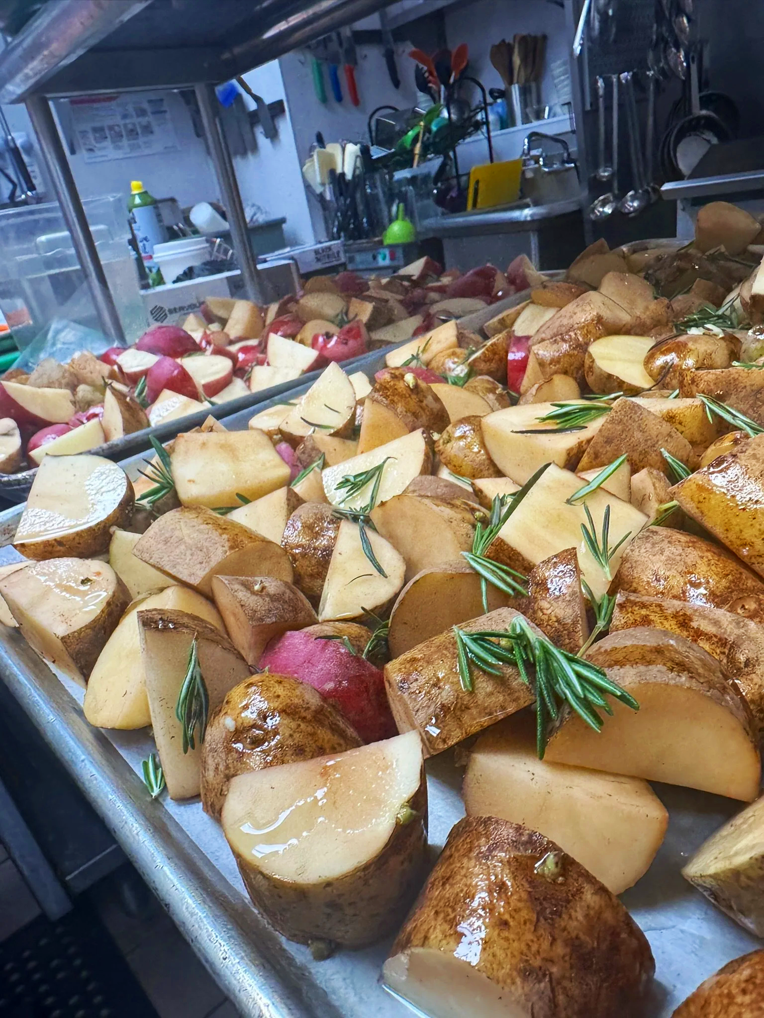A kitchen counter with chopped potatoes garnished with rosemary. In the background, knives, utensils, cutting boards, and cleaning supplies are visible.