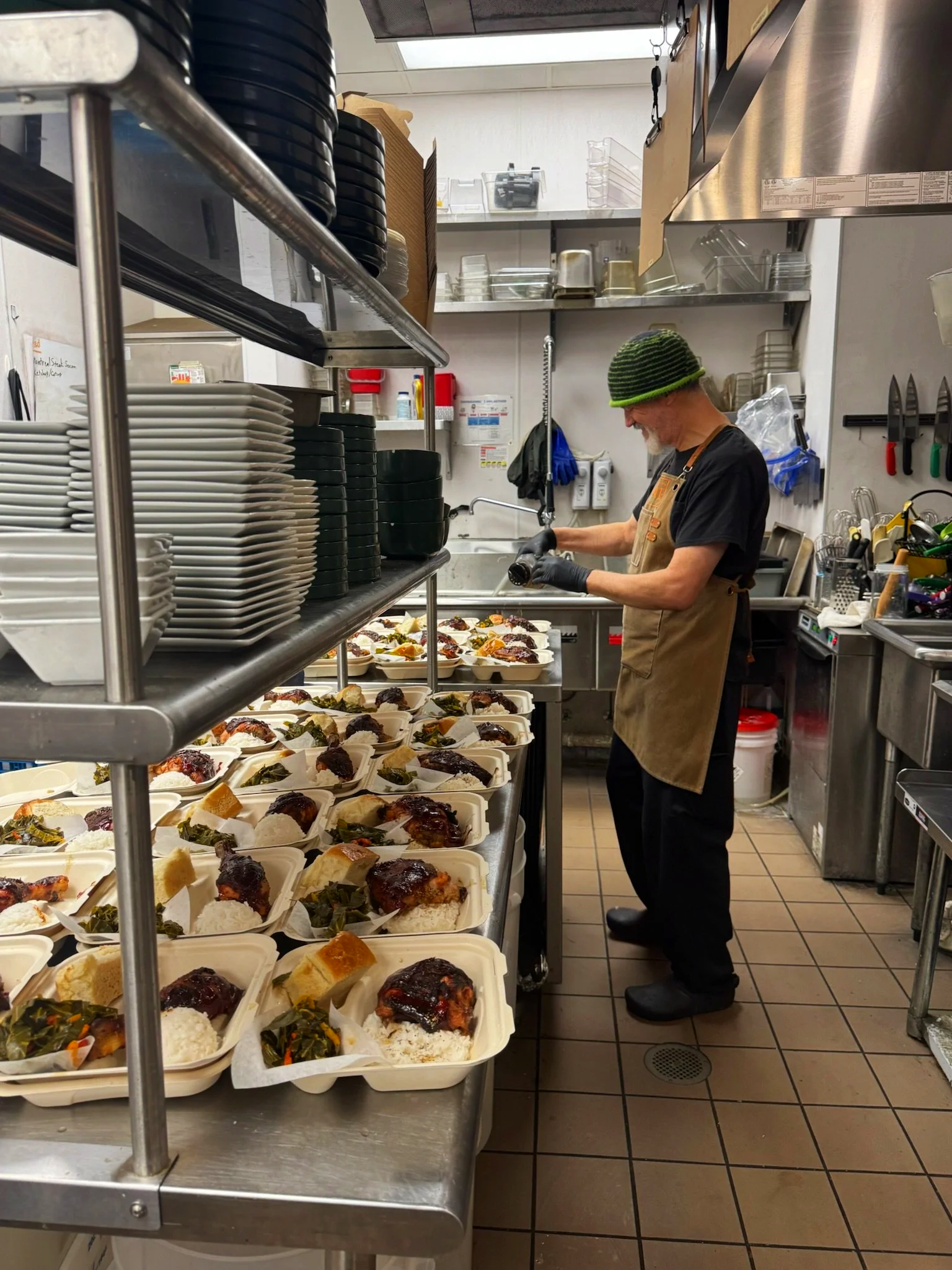 A man working in a commercial kitchen preparing meals in takeout containers.