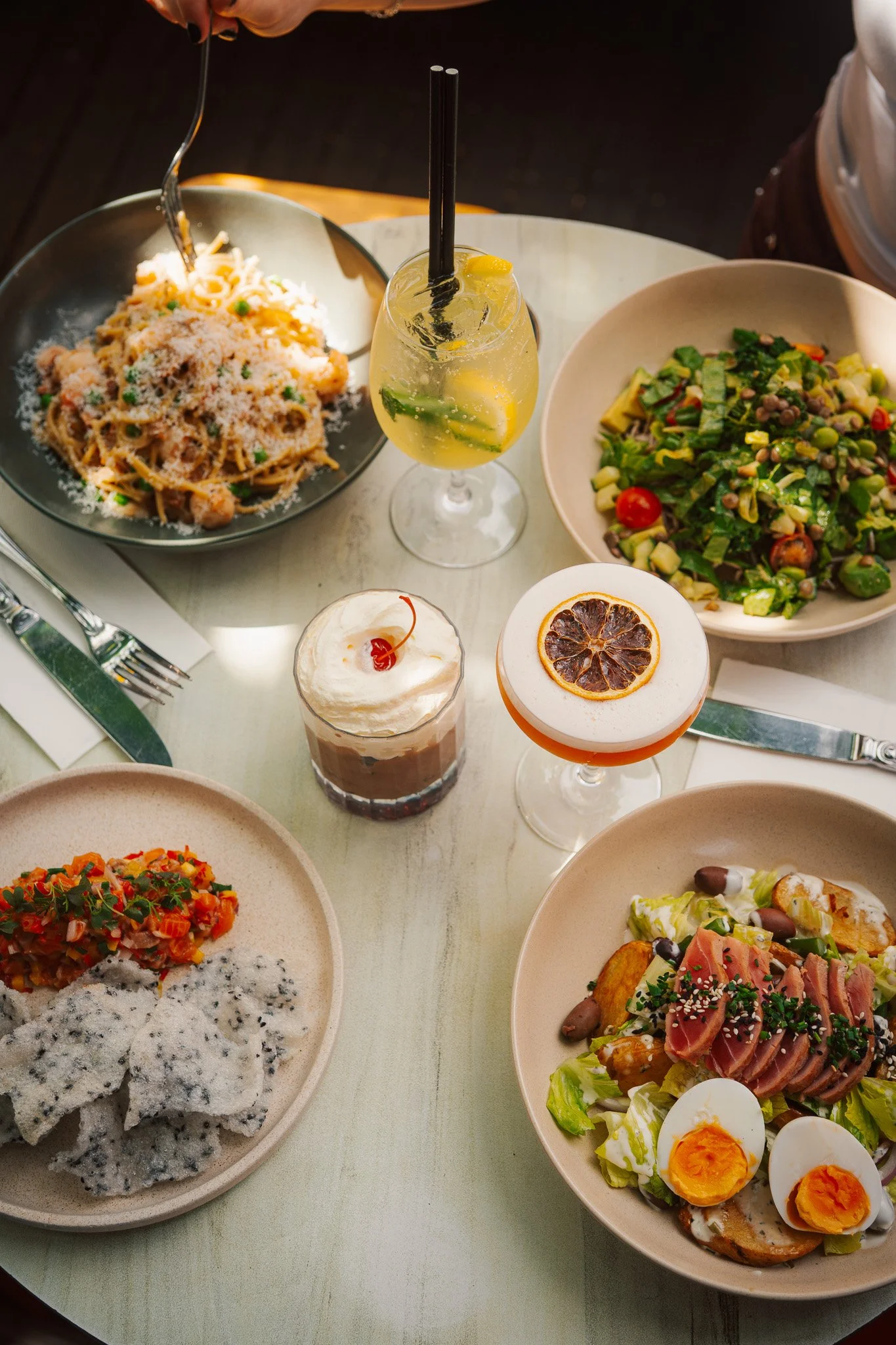 A table set with various dishes, including pasta, salads, and desserts with colorful cocktails.