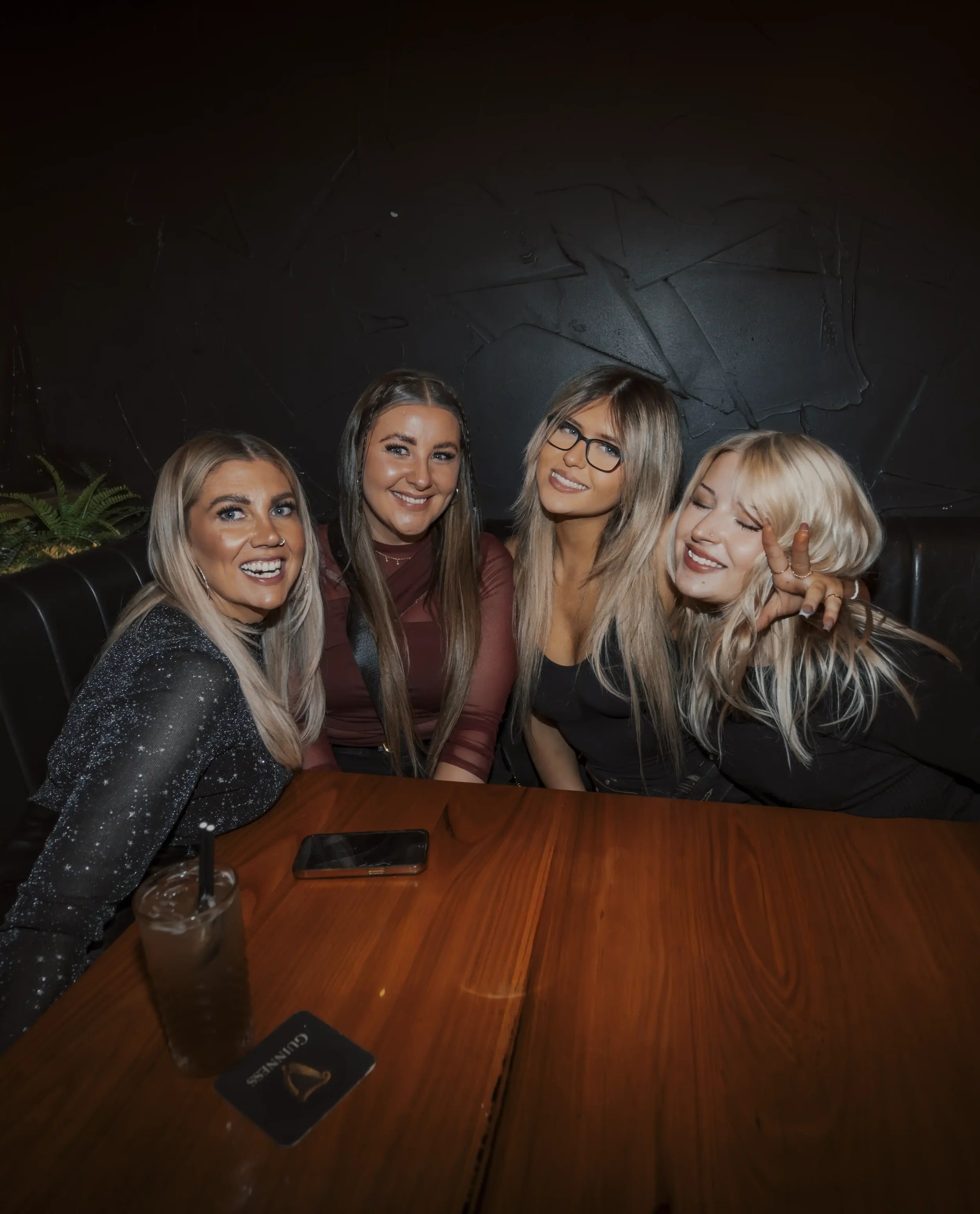 Group of people sitting in a restaurant booth under warm lighting and surrounded by plants.