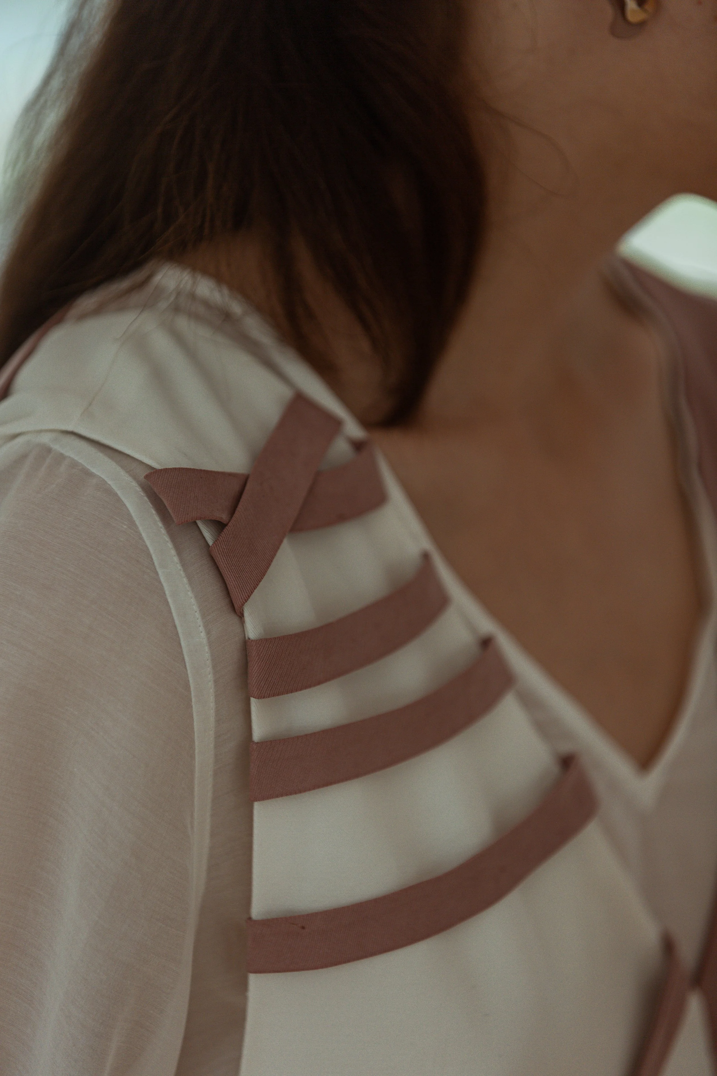 Close-up of a woman wearing a white top with brown decorative straps on the shoulder.