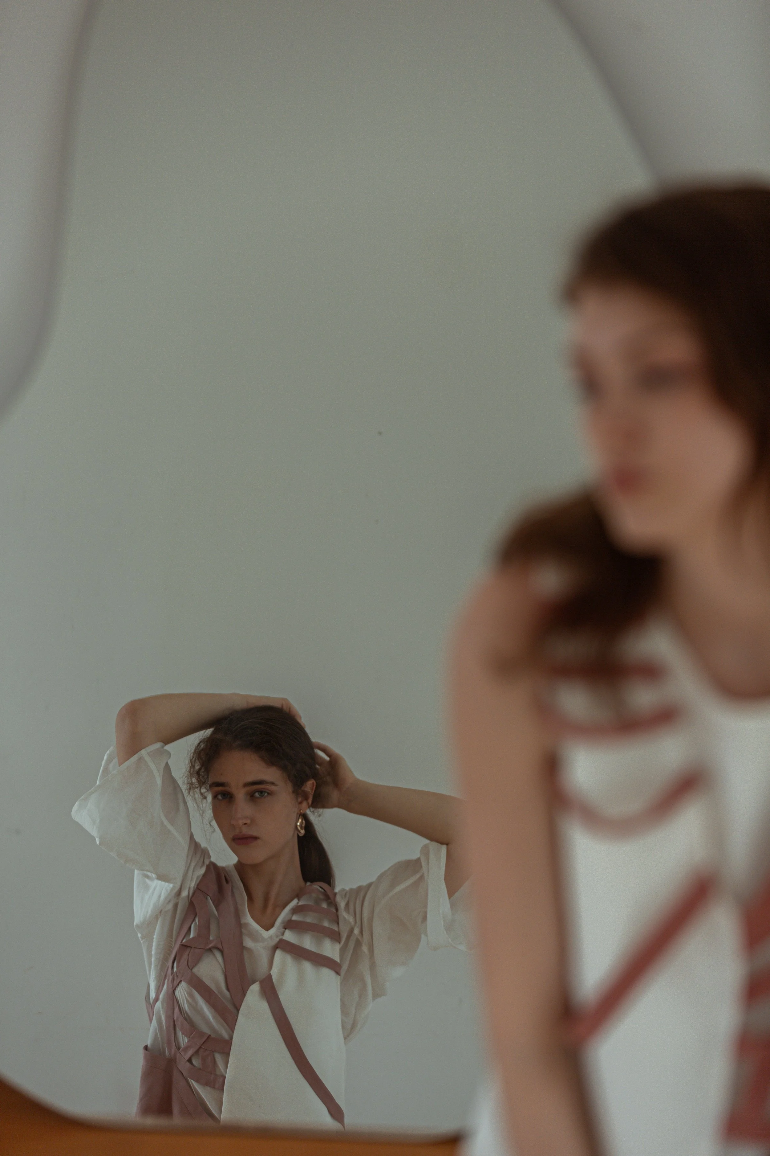 A young woman with brown hair and earrings looking at her reflection in a mirror while adjusting her hair.