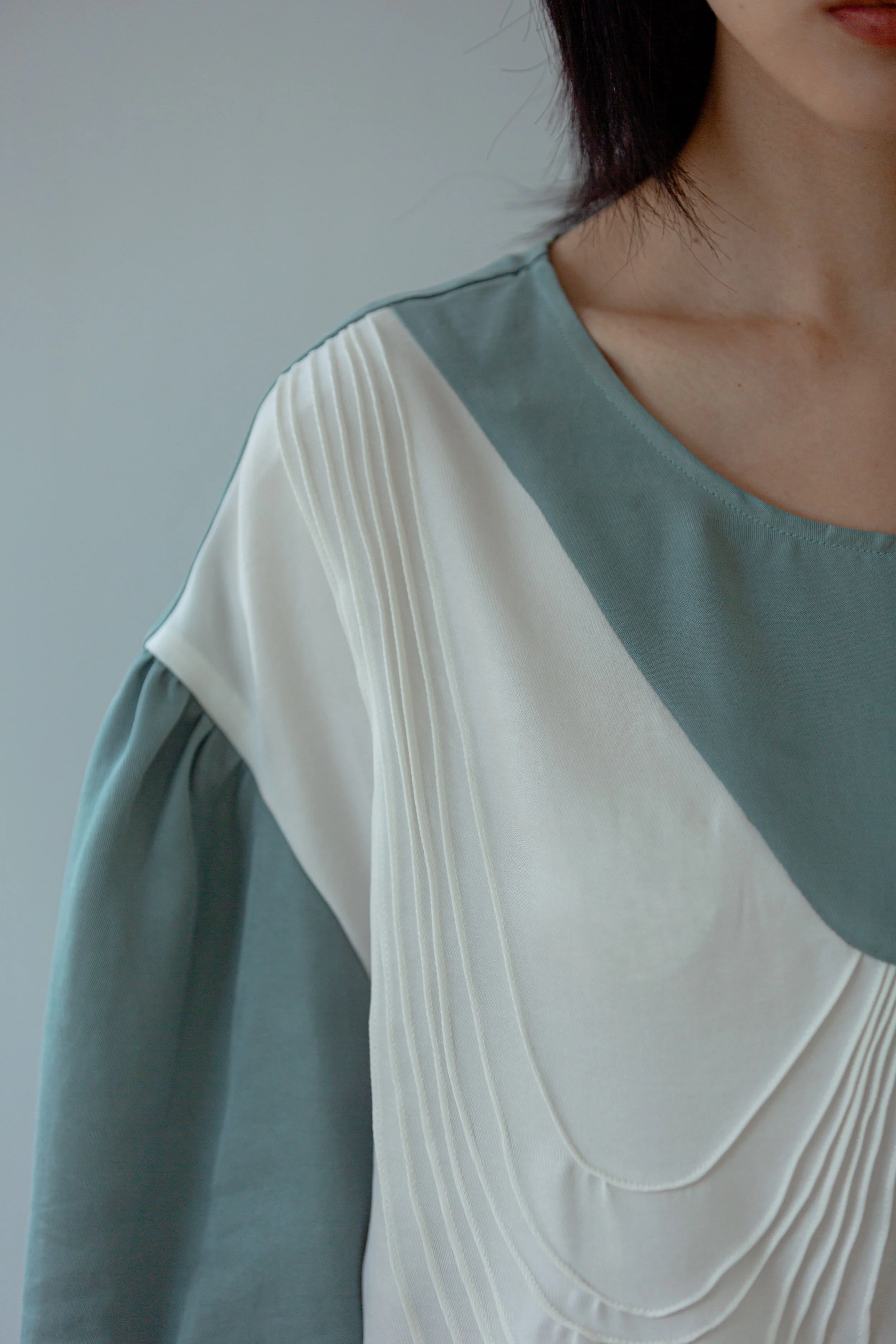 Close-up of a woman wearing a stylish top with color-blocking pattern and pleated details on the front near the shoulder.