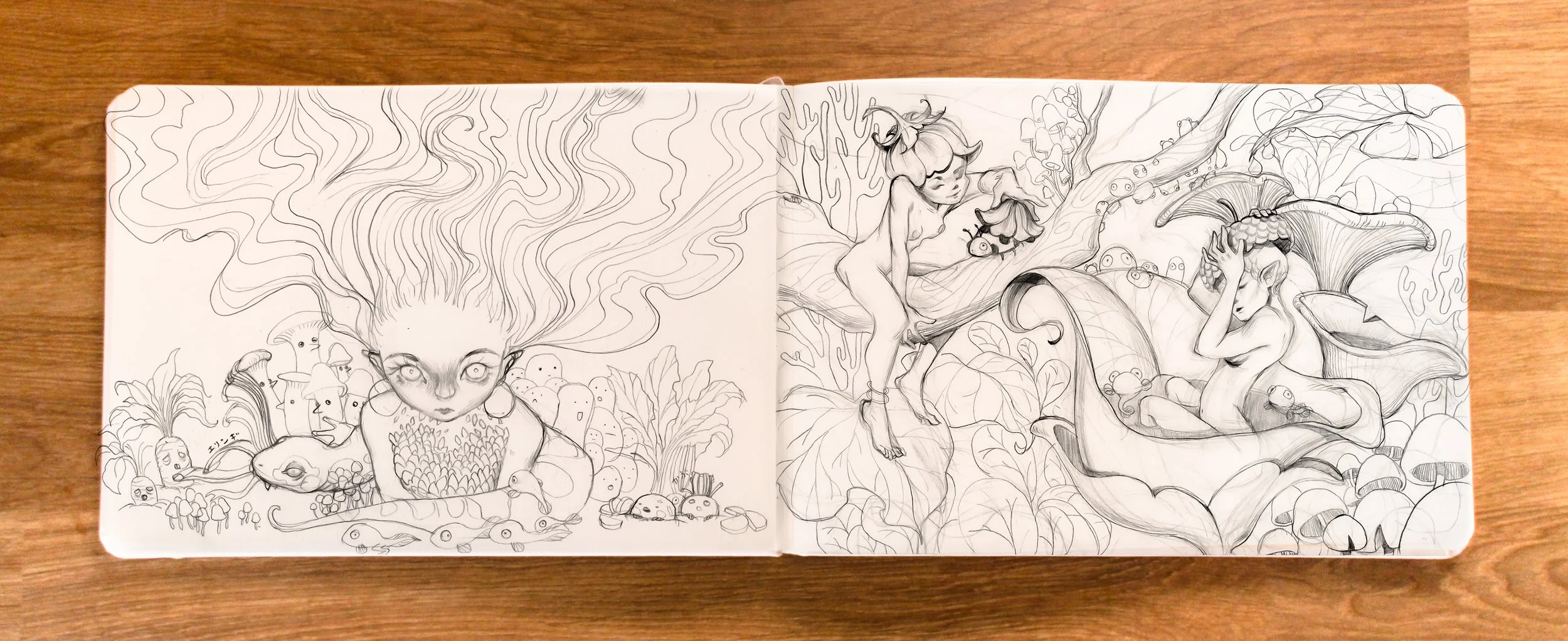 A sketchbook open to a two-page illustration of fantasy scenes. The left page has a girl with flowing hair and luminous eyes, surrounded by mushrooms, small creatures, and plants. The right page features a fairy-like character sitting on a large leaf