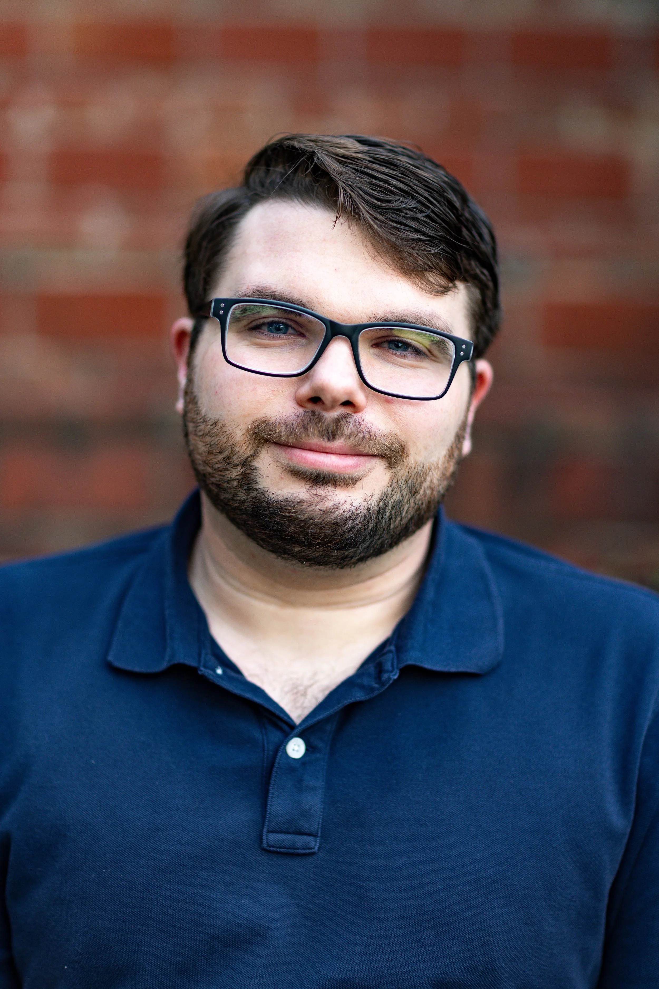 Moody and cinematic editorial portrait photography of a man with glasses against a brick background in Richmond, Virginia.