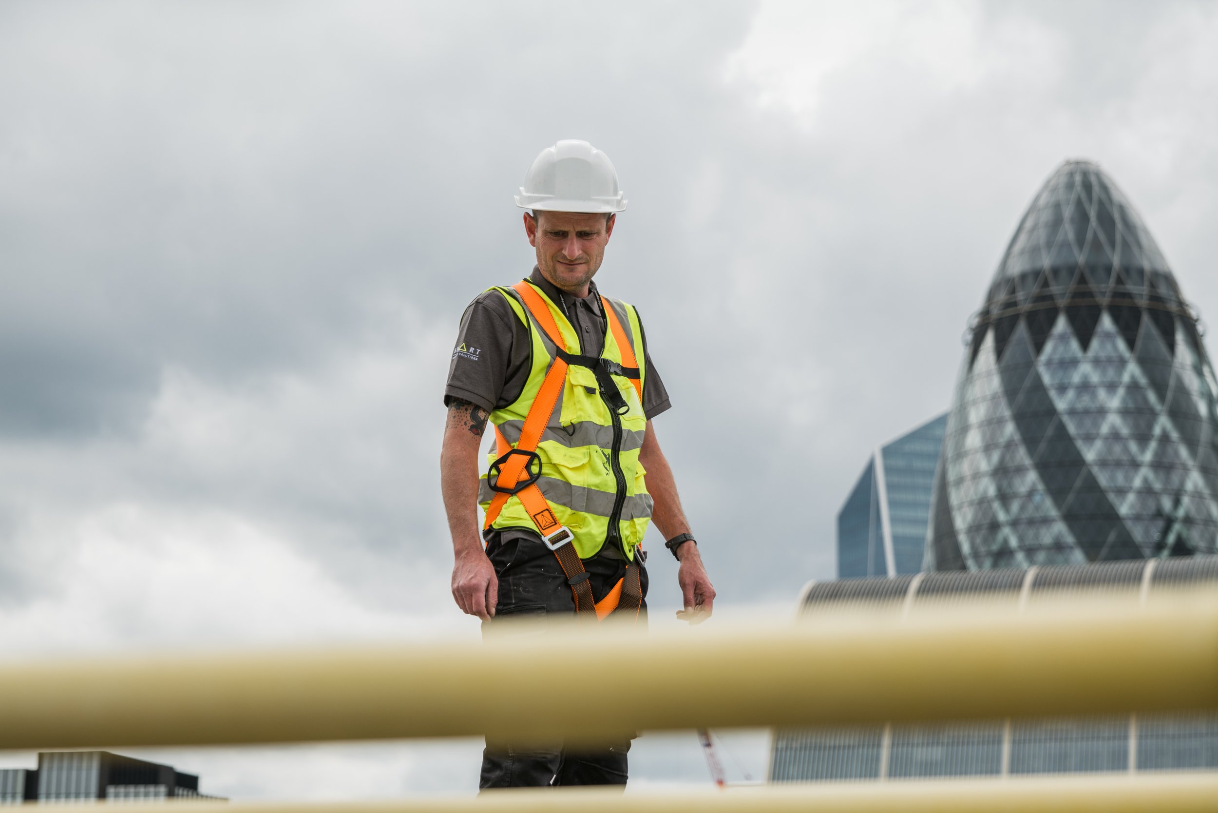 Business lifestyle portrait of a Construction worker with safety gear and helmet on rooftop, iconic building in background