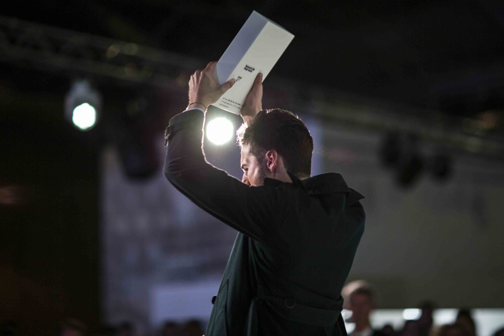 Person holding award plaque overhead on stage