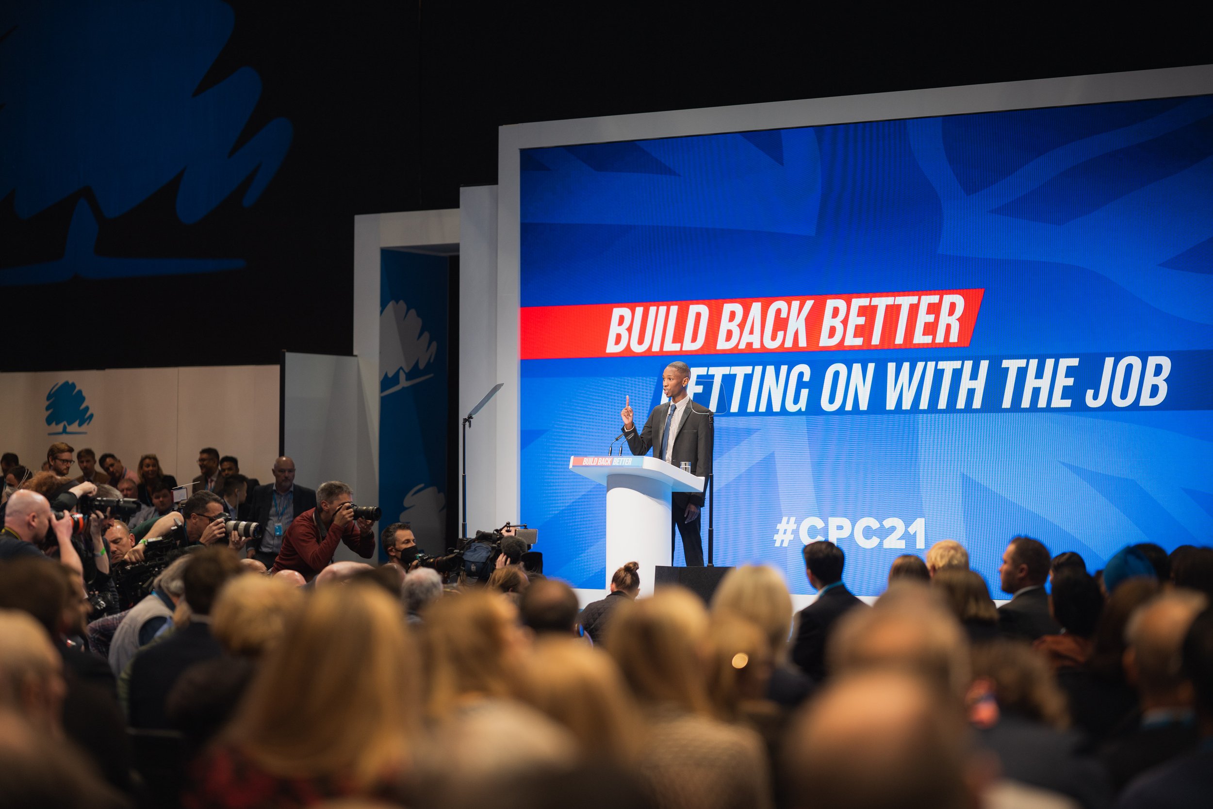 Speaker at a podium during CPC21 with "Build Back Better" message on screen