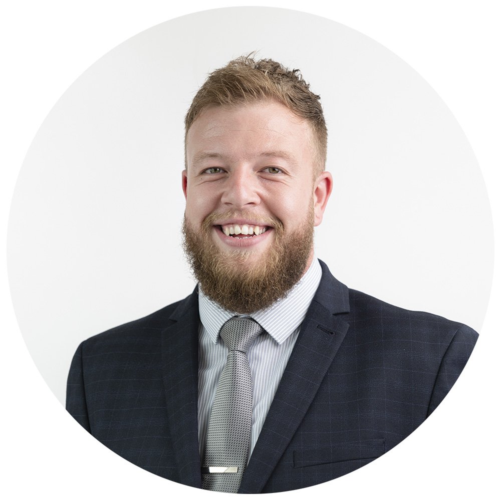 Corporate headshot of a man in business suit smiling with beard, wearing a striped shirt and tie against a white background.