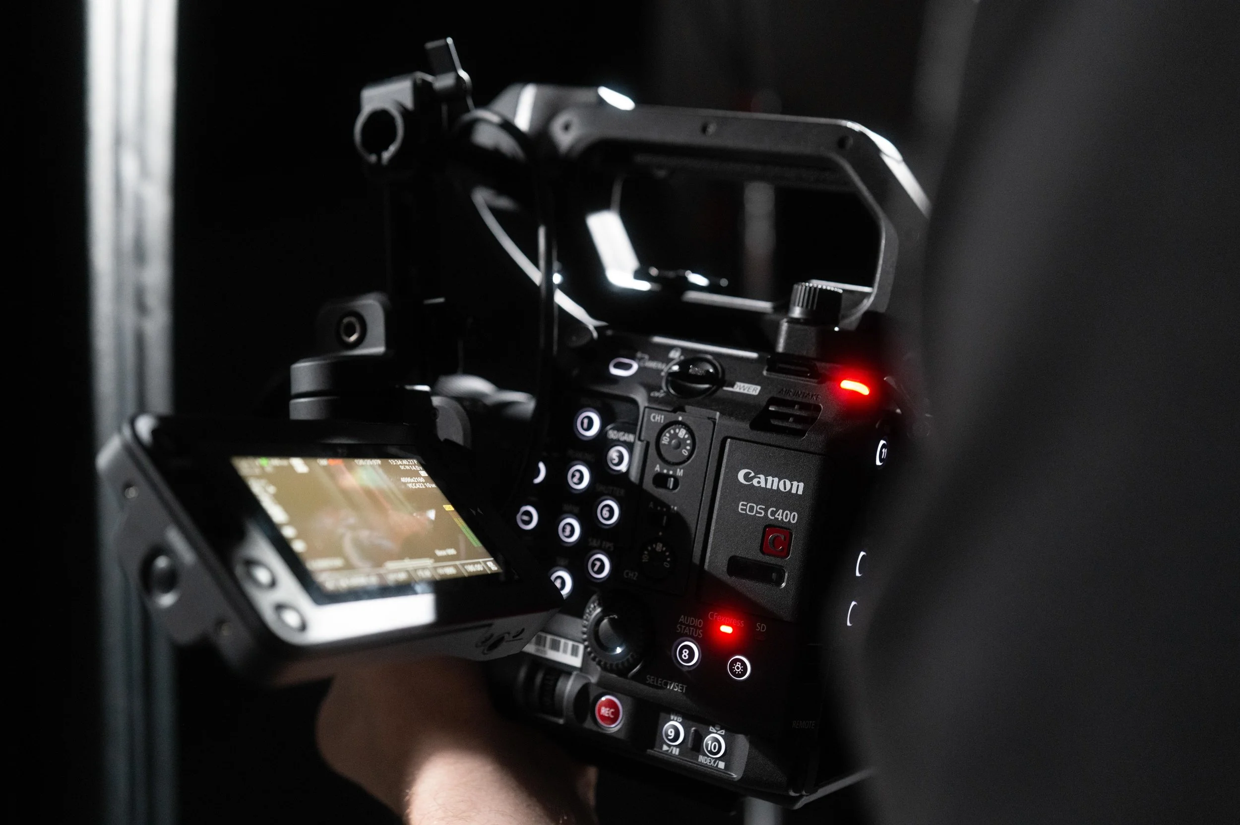 Close-up of a Canon EOS C400 camera with an attached monitor, being operated in a dark setting.