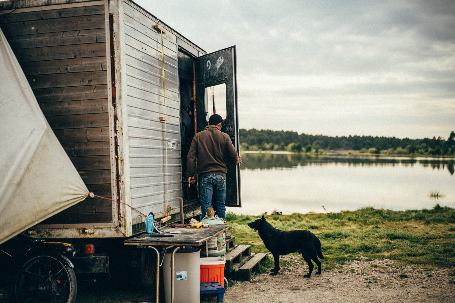  Un jeune homme vit dans un camion au bord d'un lac d'un village isolé en périphérie de Bordeaux. Une bénévole vient lui porter des chèques services. Avec Caritas France. Martillac, le 7 avril 2020 // A young man lives in a truck by a lake in a remot