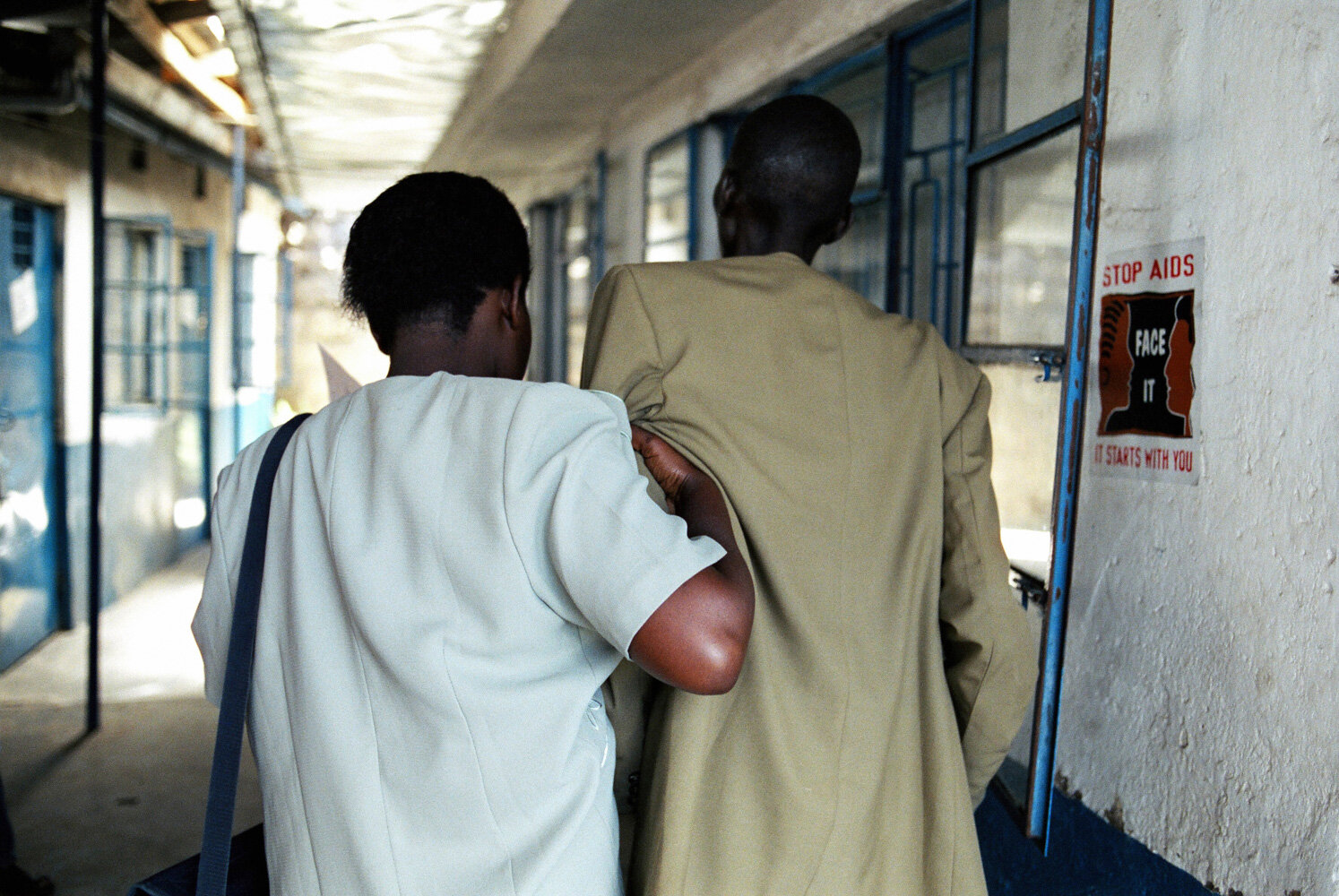  Un couple entre dans la clinique SIDA du bidonville de Matharé pour se faire dépister. La femme soutient son mari, trop faible pour marcher seul. Avec Médecins Sans Frontières, dans la lutte pour l'accès aux médicaments essentiels. Nairobi, Kenya. M