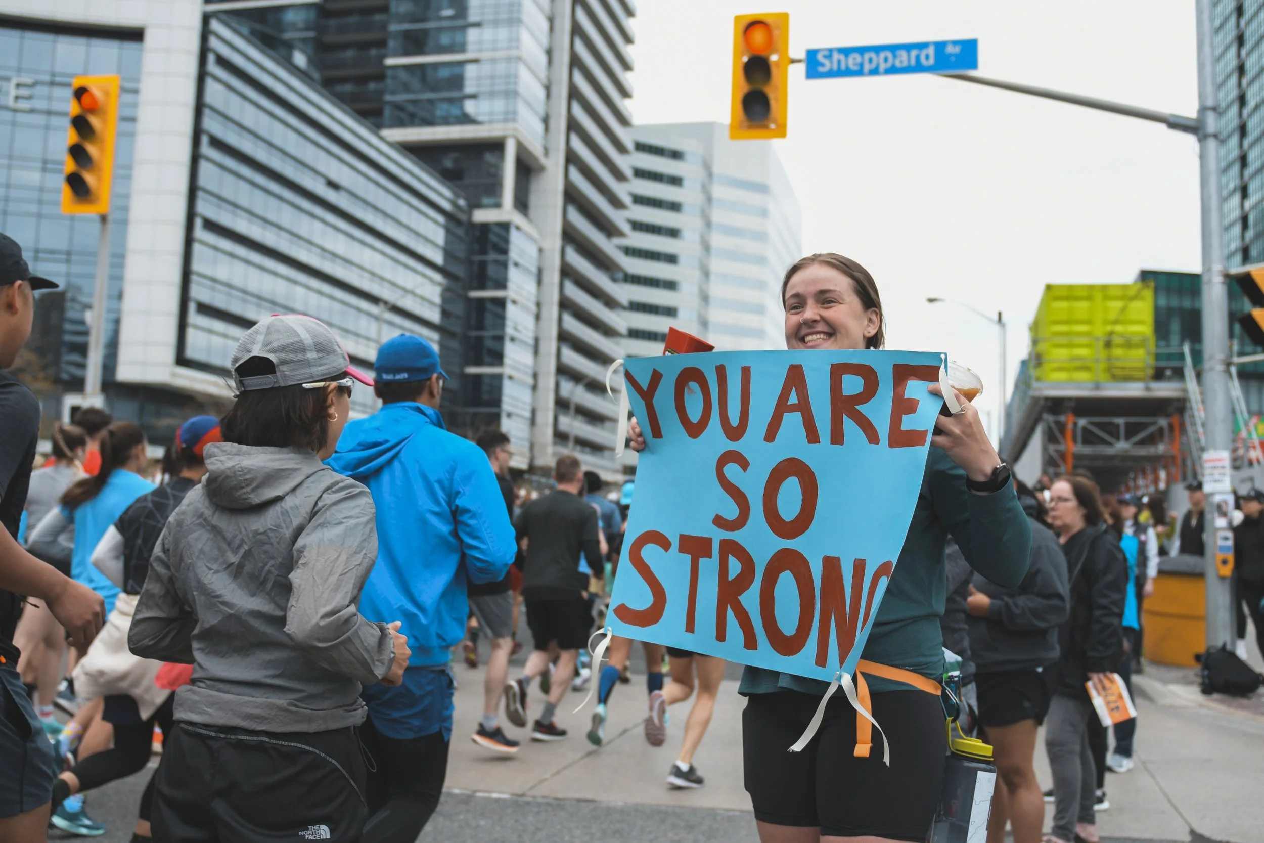A supporter holds a sign with a smile as runners pass during the Toronto Marathon. May 7, 2023. (Kaj Larsen photo for Marathonfoto/Toronto Marathon)