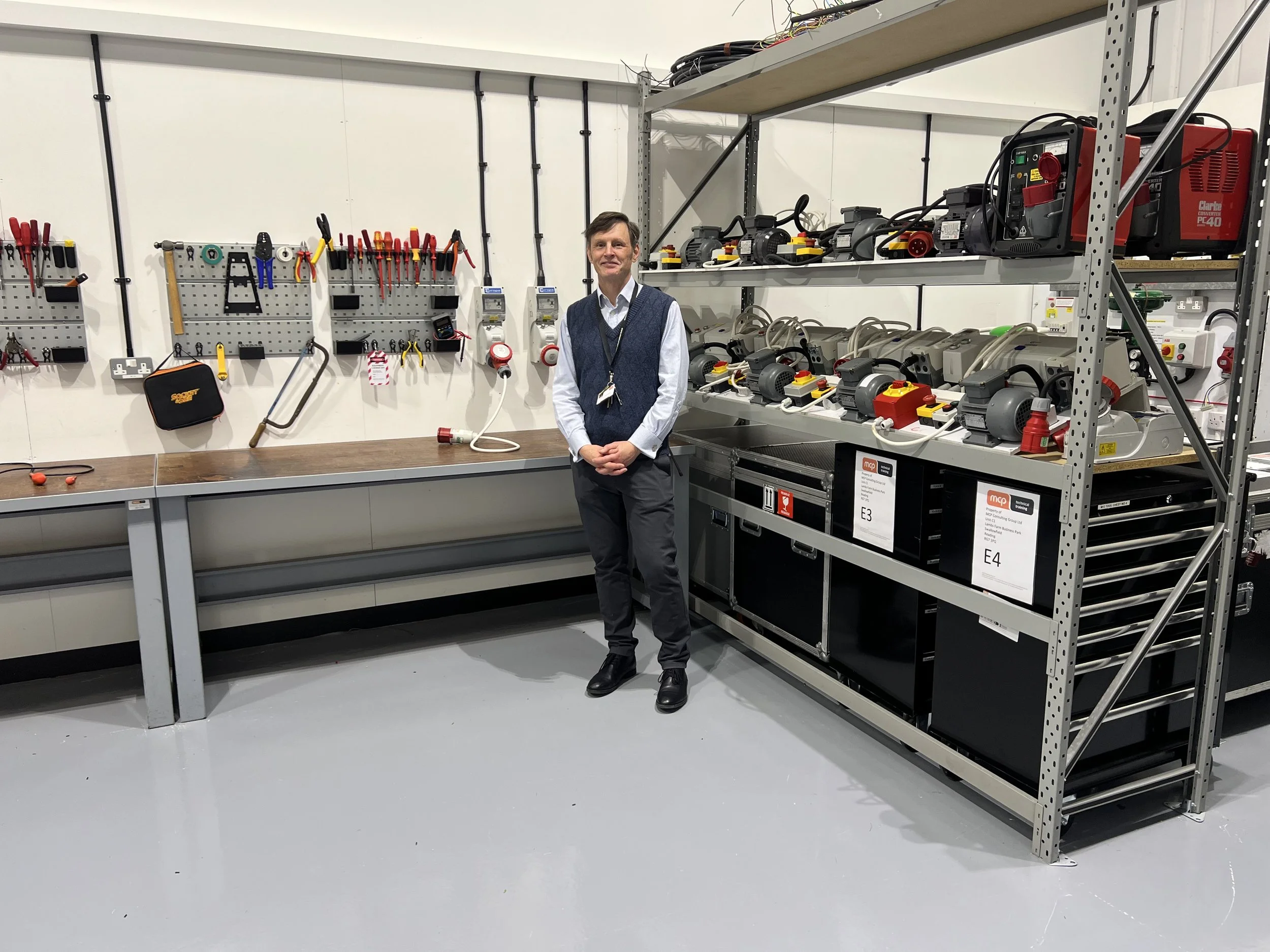 A man standing in a workshop next to shelves with various tools and machines.